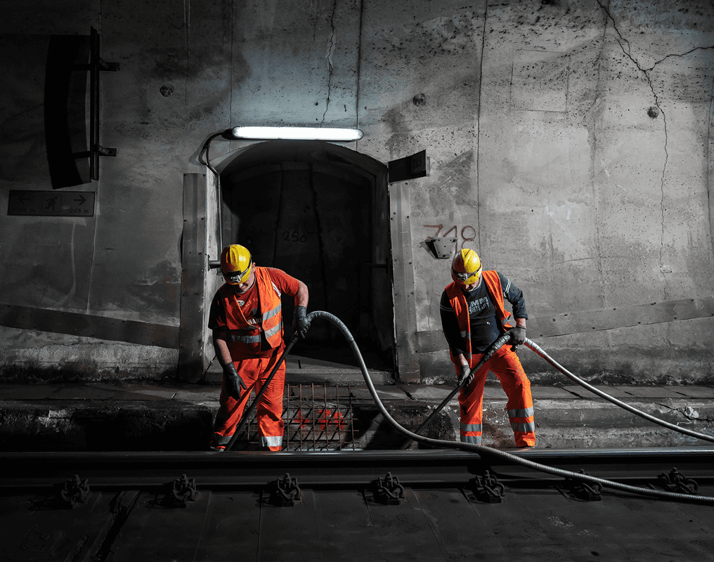 Due operatori in abbigliamento ad alta visibilità che lavorano su binari ferroviari in ambiente sotterraneo
