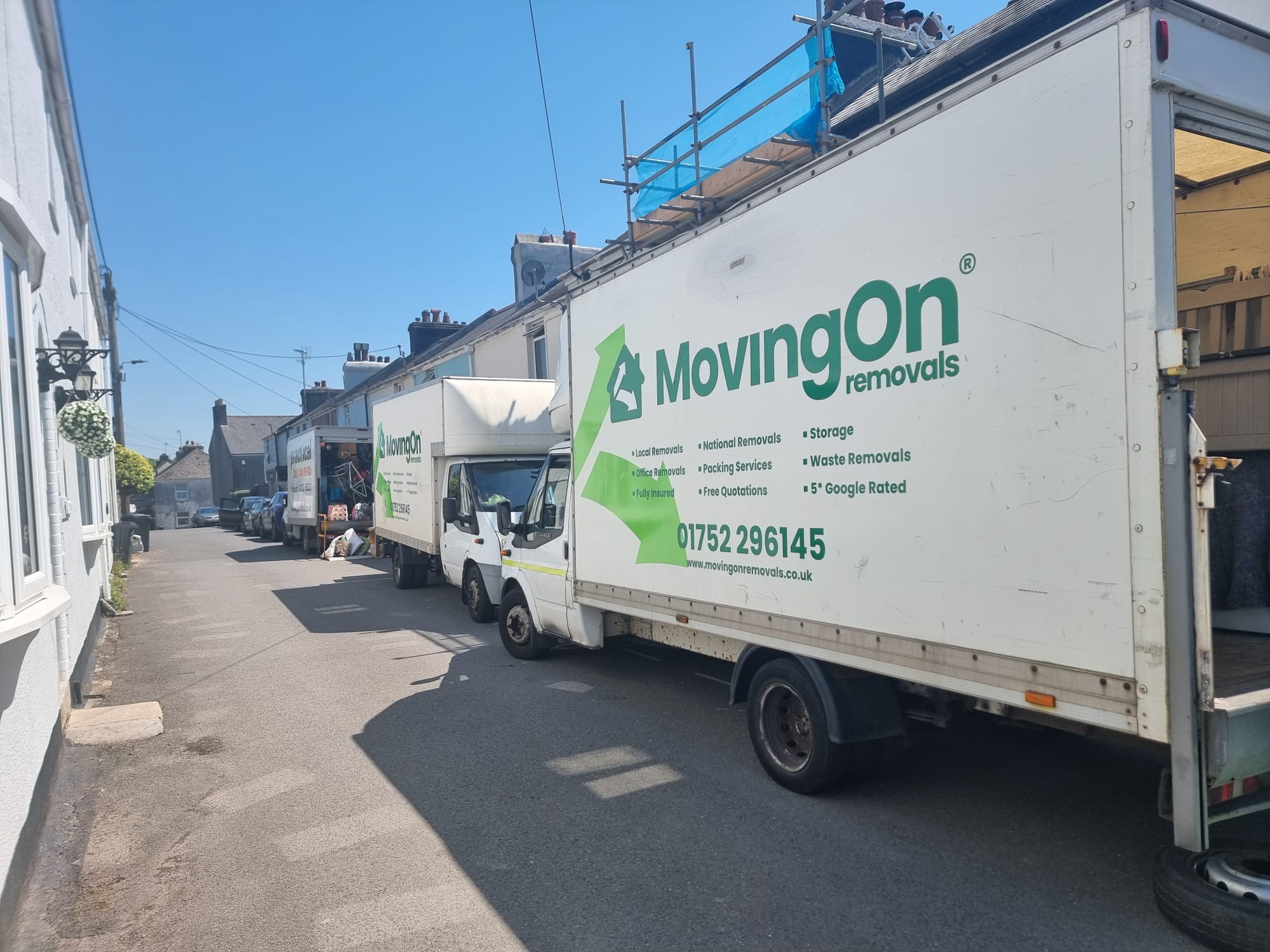 Three large Moving On Removals transit vans parked in a row on a residential street during a large house move from Ivybridge to Stoke, Plymouth.