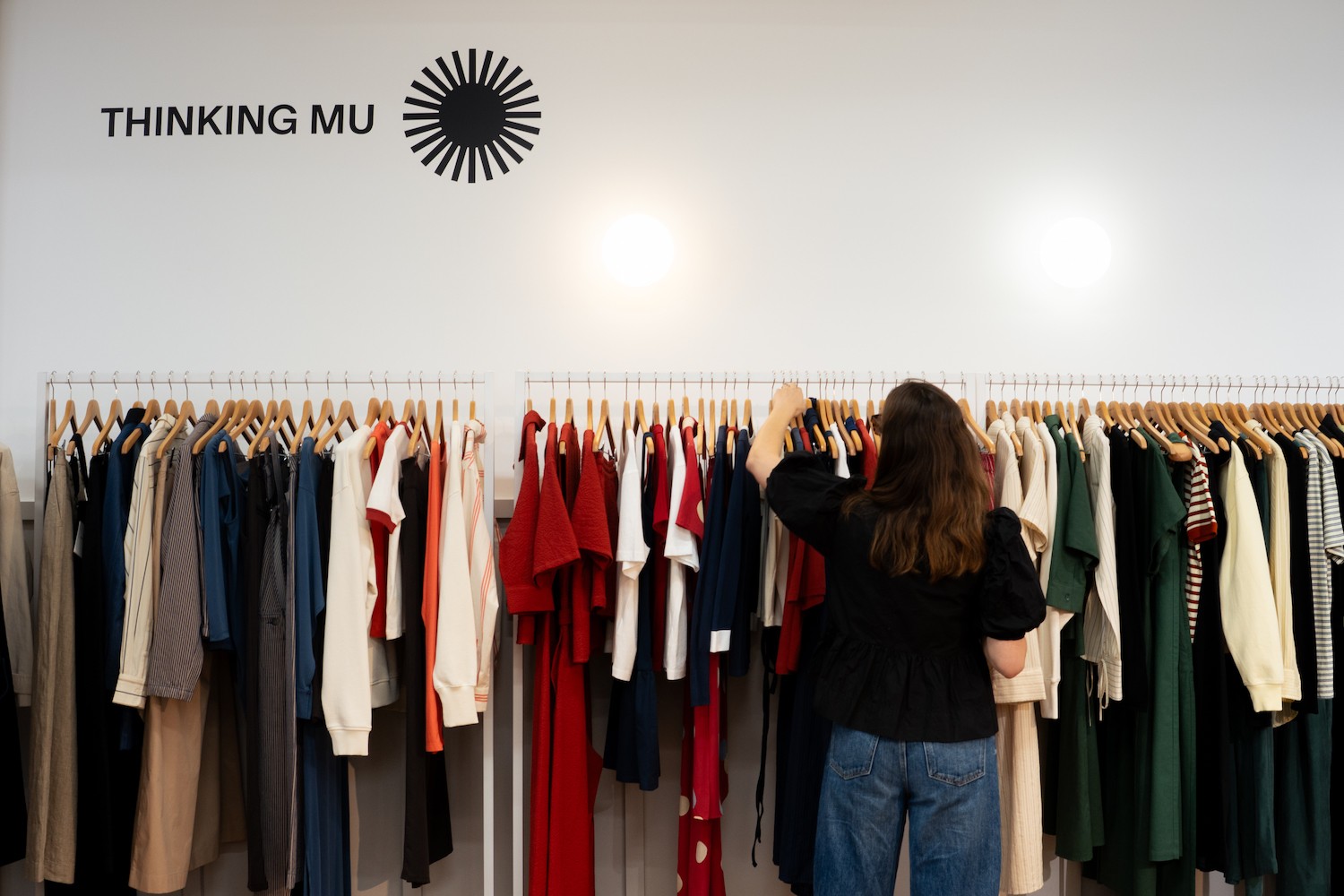 Une femme choisit des pièces sur un portant avec la marque Thinking Mu visible