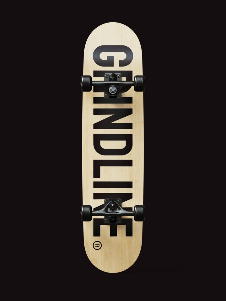 Top-view skateboard deck on black, natural wood finish with “GRINDLINE” in bold black letters running lengthwise down the centre.