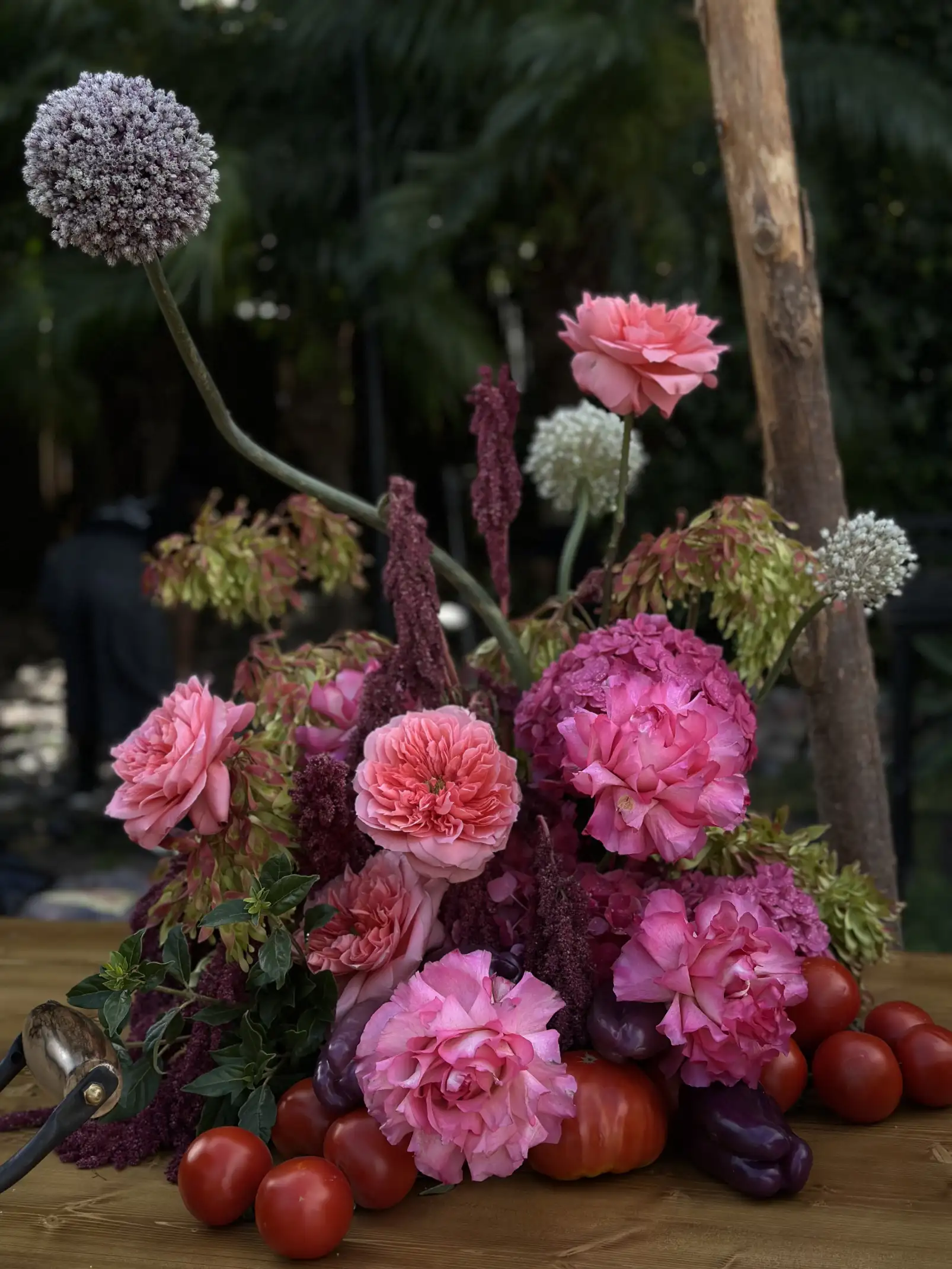 Arreglo floral con rosas rosadas, tomates y pimientos para instalación botánica creativa, combinando flores y vegetales en composición artística.