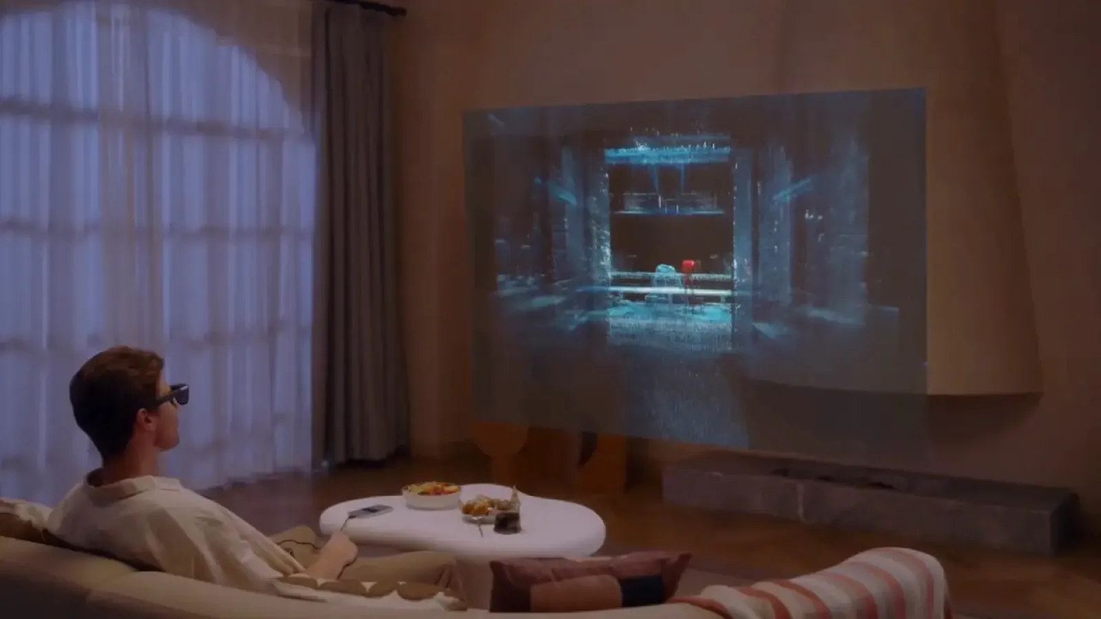 A person sits on a modern couch in a dimly lit living room, wearing 3D glasses and watching an immersive 3D movie projected onto a large wall screen, with snacks on the sleek coffee table in front.