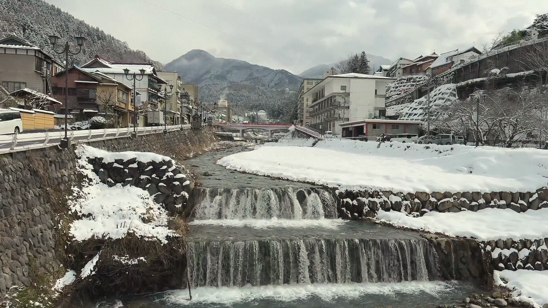 Snow-covered rooftops and the stepped weir of the Yokoyu River running through Shibu Onsen in winter, Yamanouchi