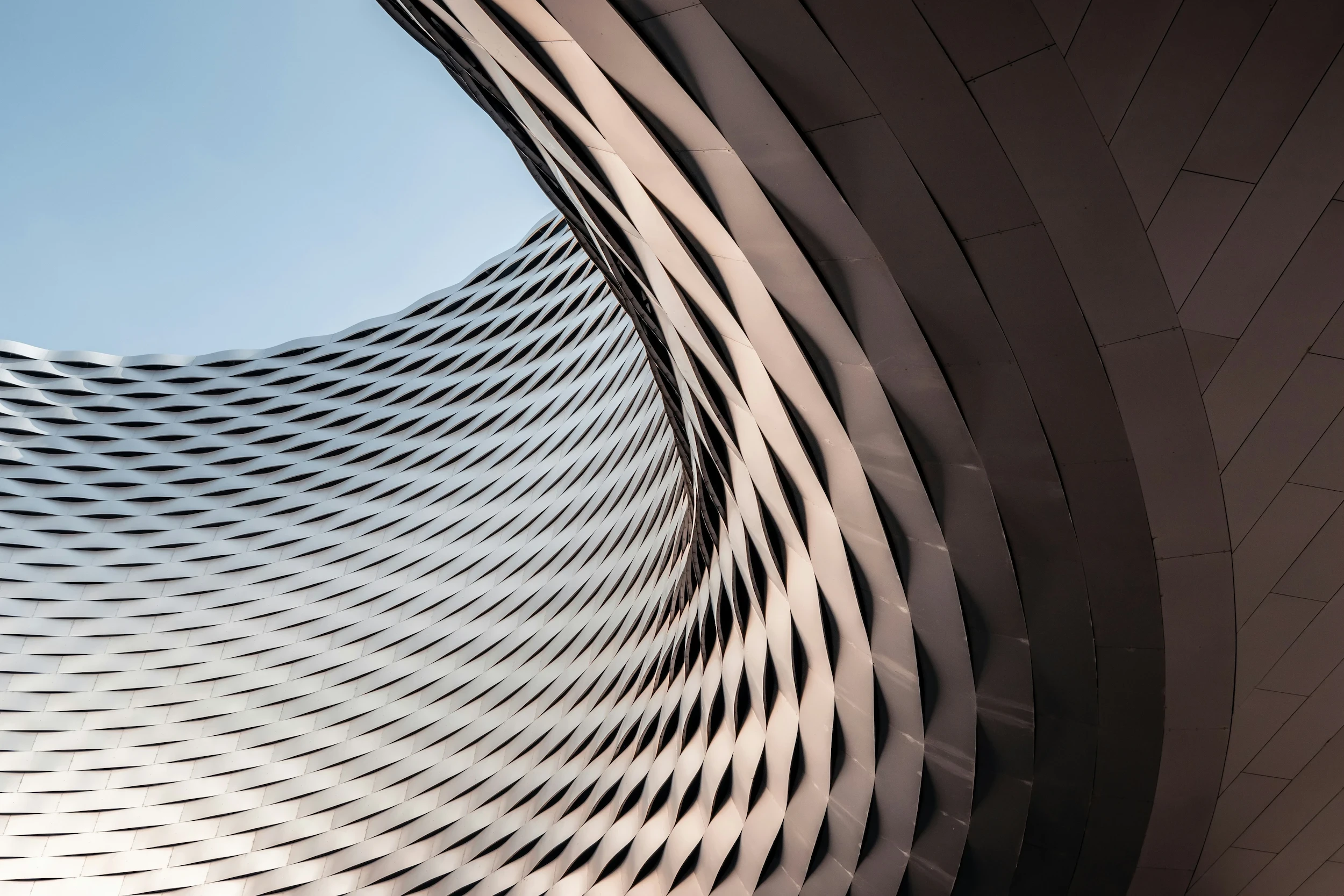 Close-up abstract view of a swirling, metallic architectural facade with a complex, textured basket-weave pattern and deep shadows.