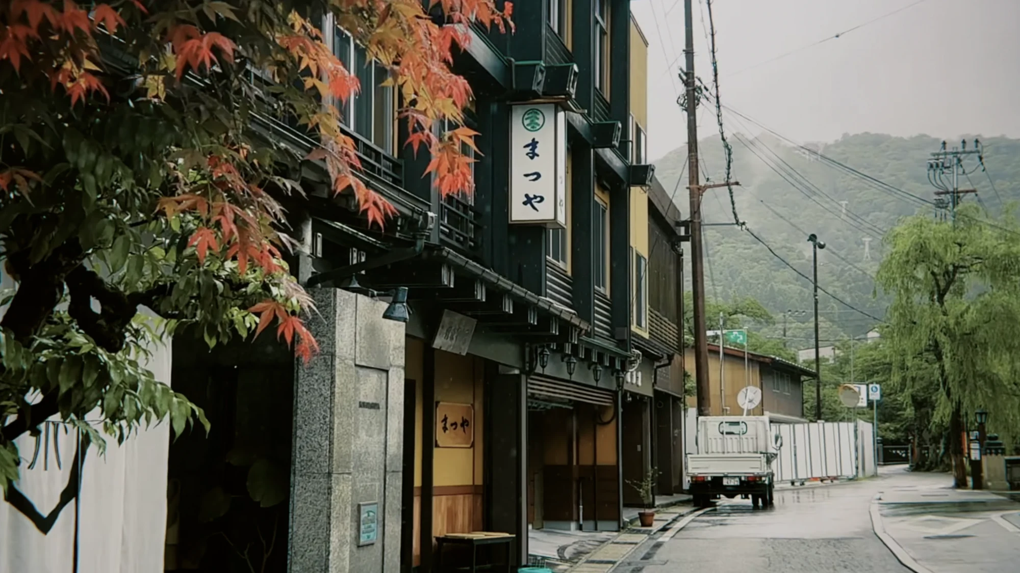 Red maple branches over a Kinosaki street with an inn frontage behind.