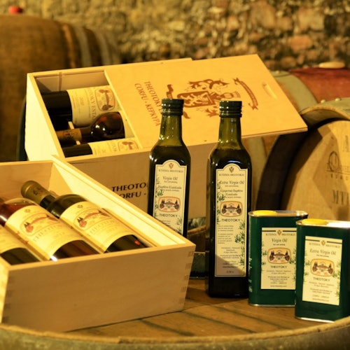 木製箱子裡裝著葡萄酒瓶、兩瓶橄欖油和兩罐橄欖油，放置在一個木桶上，背景帶有鄉村風格。