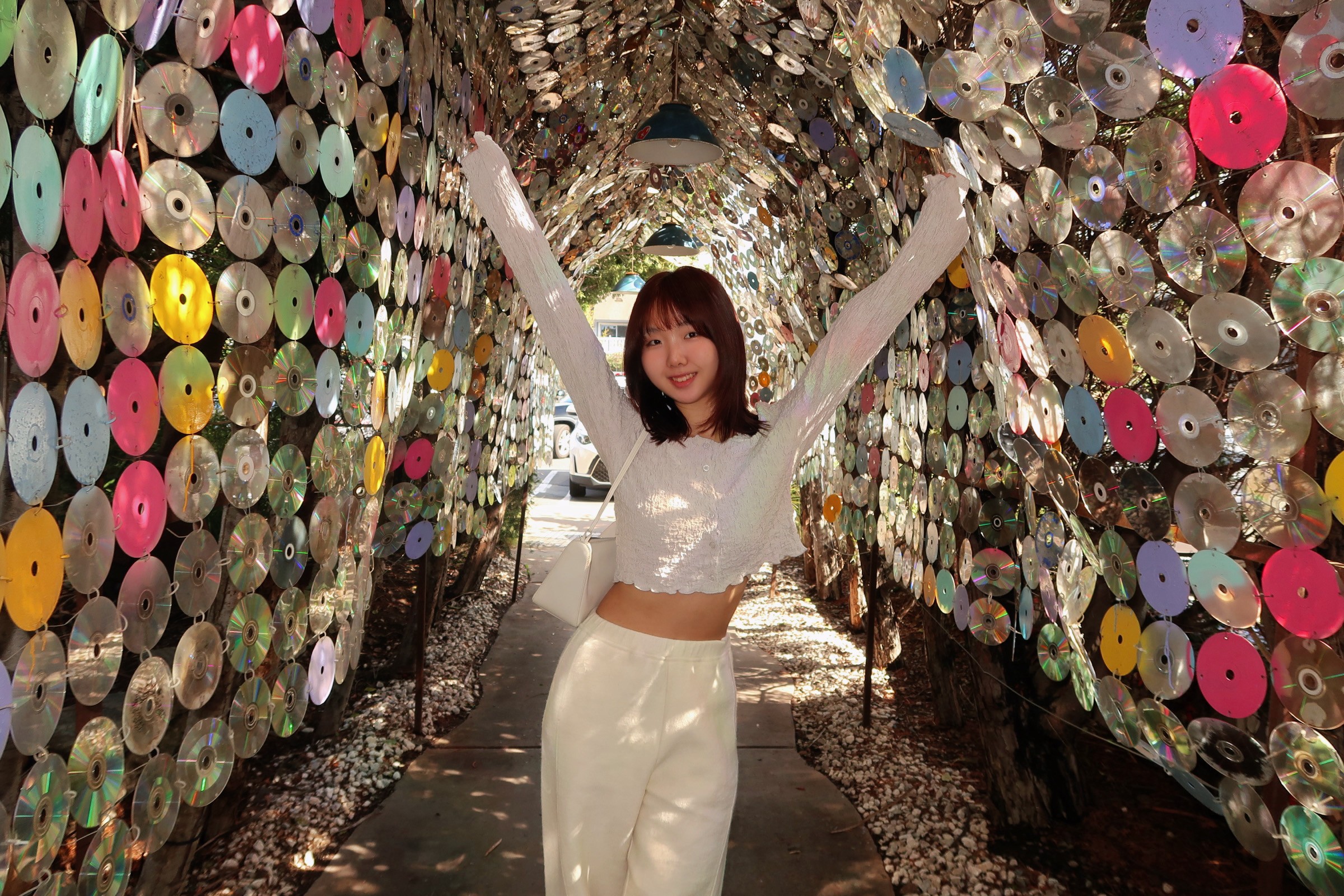 Una persona con una camiseta negra y pantalones de color claro está de pie en la cima rocosa de una montaña al atardecer, sosteniendo una cámara frente a su cara para tomar una foto. Un mar de nubes se extiende detrás de ellos, iluminado por la luz dorada del sol poniente.
