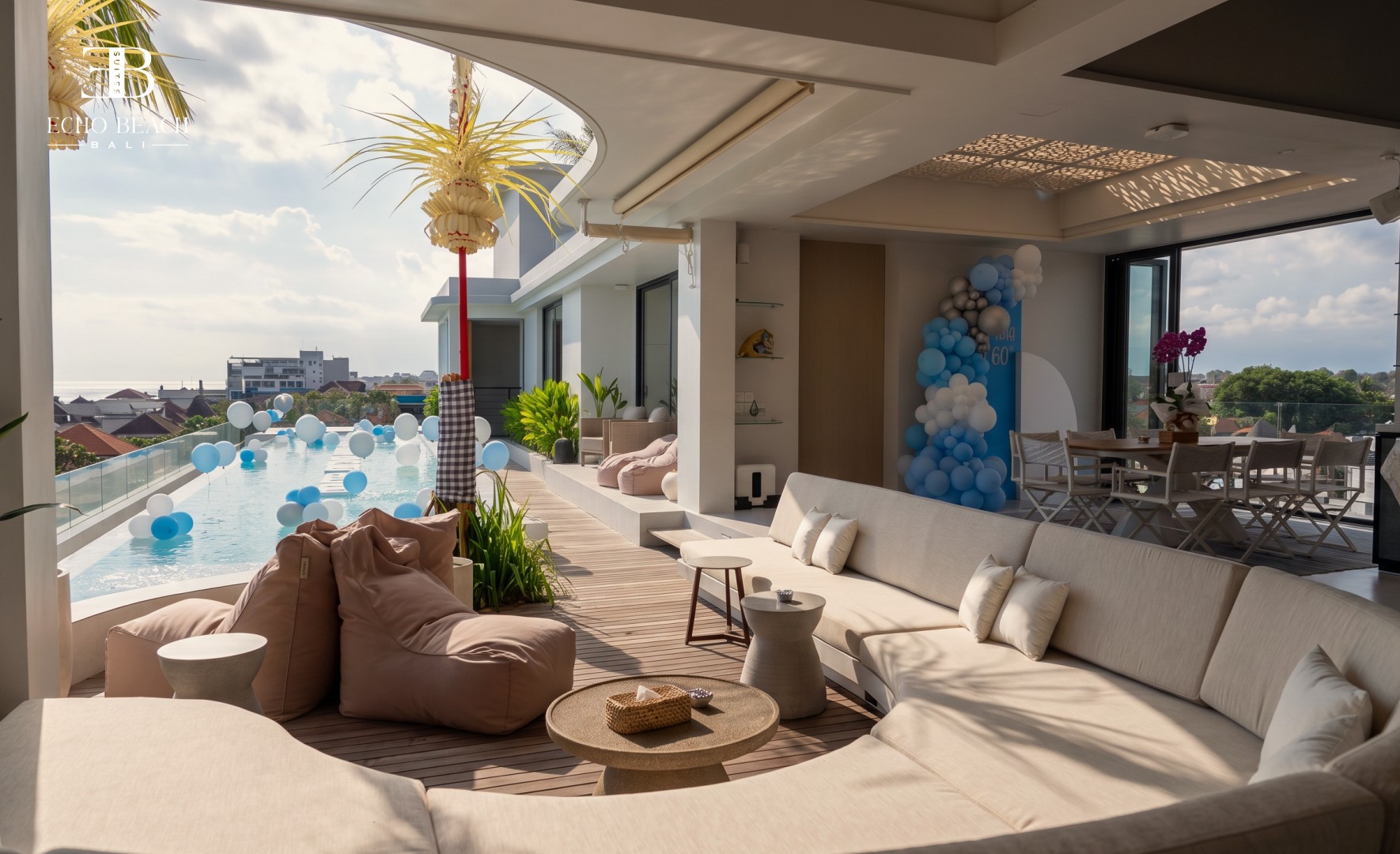 Open-plan kitchenette and dining area featuring a wooden table and bench, a refrigerator, and unique pendant lighting, leading to the bedroom at the Echo Beach Suite in Canggu, Bali.