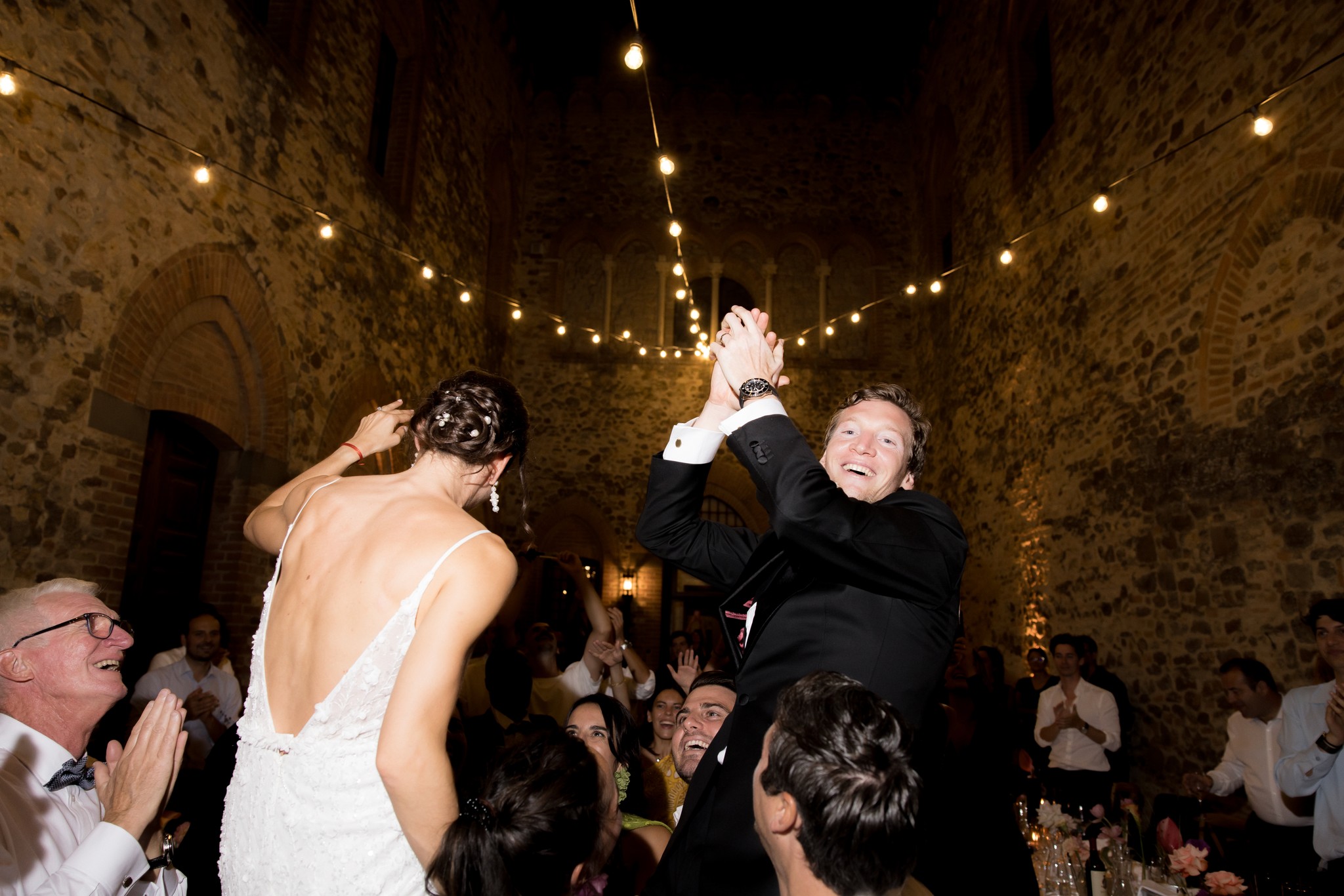 Sposi sollevati tra gli ospiti al ricevimento del Castello di Tabiano, festeggiamenti sotto le volte illuminate