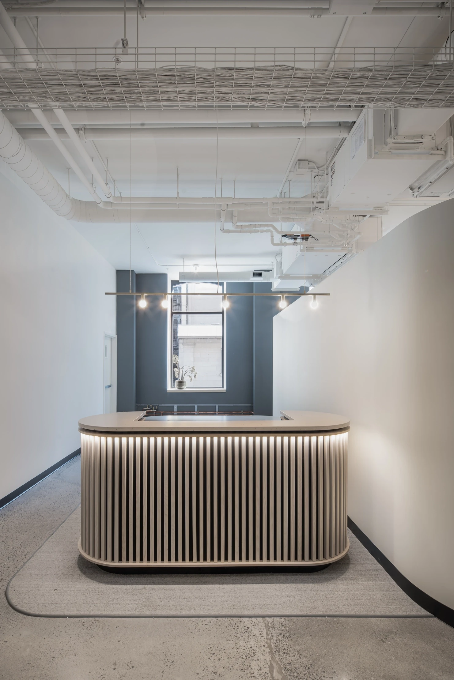 Minimalist reception desk at Dialogue, framed by soft lighting and a sculptural wood panel design, creating a refined welcome area.