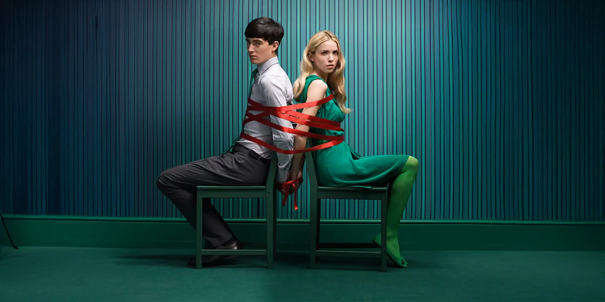 Two people seated back to back, bound together with red tape, symbolising organisational tension, constraint, and resistance to change.