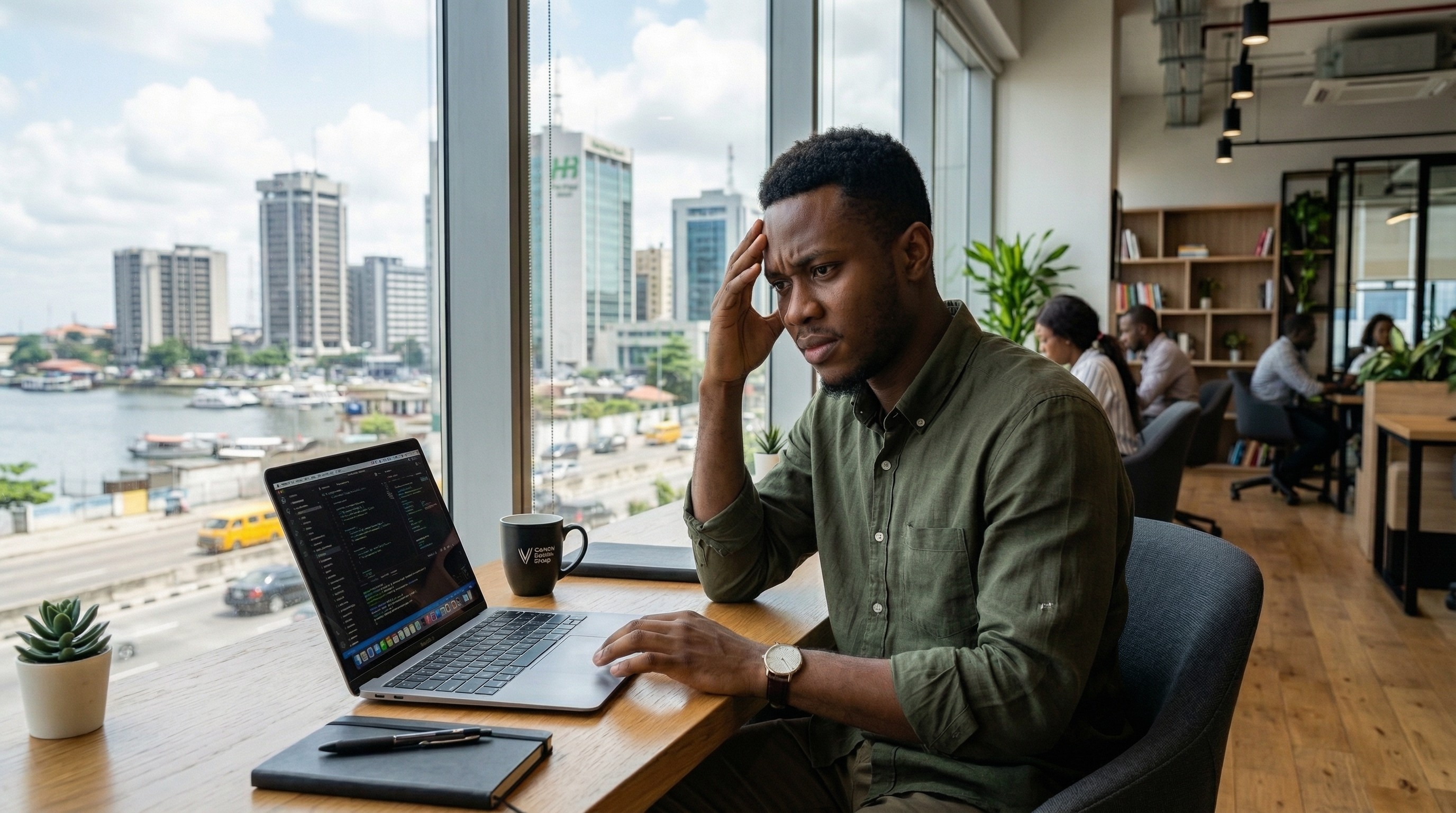 A young African startup founder sitting at a co-working space in Lagos, looking worried at his laptop screen with his hand on his forehead
