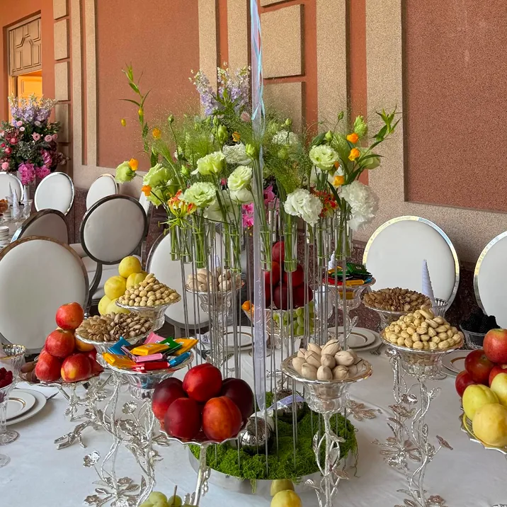 Festive banquet table with tall floral centerpiece, fruits, nuts, and candies in a luxurious setting.