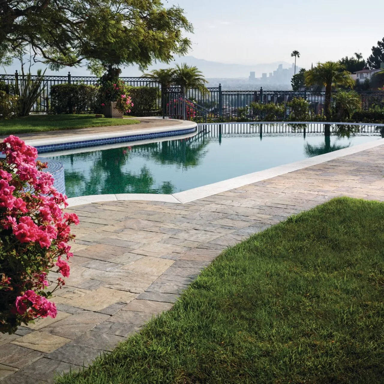 A garden pool setting Paved pool surround bordered by green lawn, flowers and a garden fence.