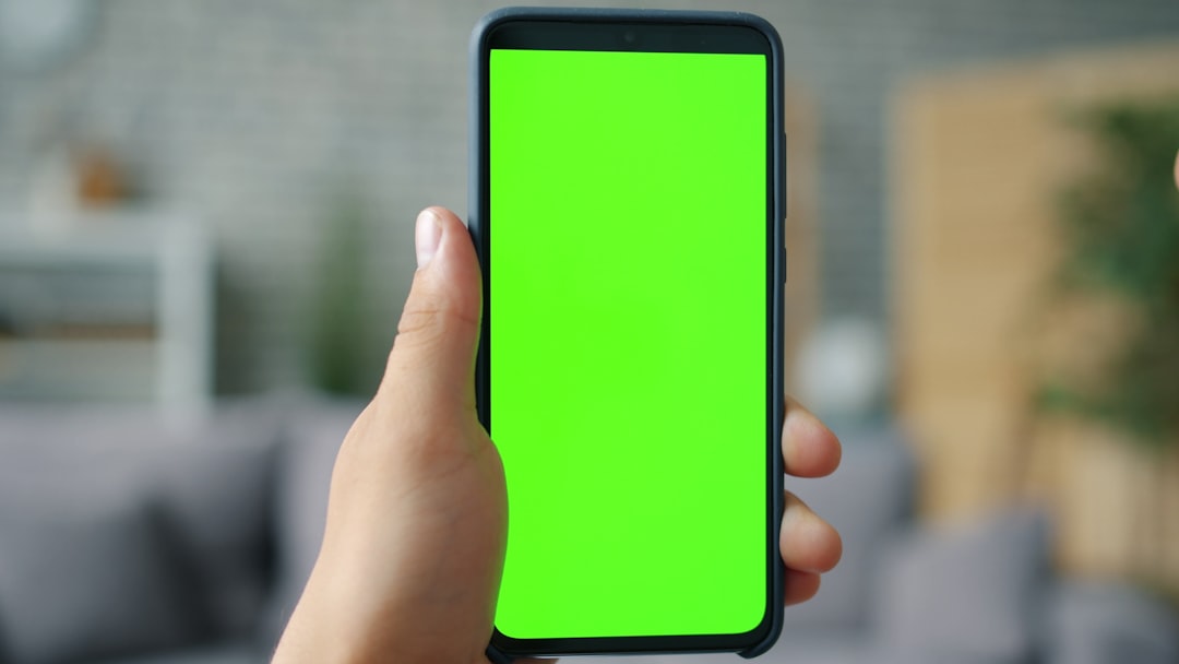 Hand holding a smartphone with a green screen.