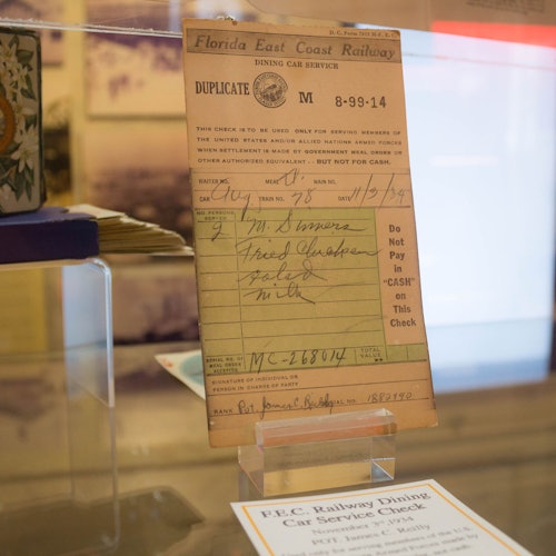 An old Florida East Coast Railway dining car service check displayed in a glass case with a typed and handwritten form.