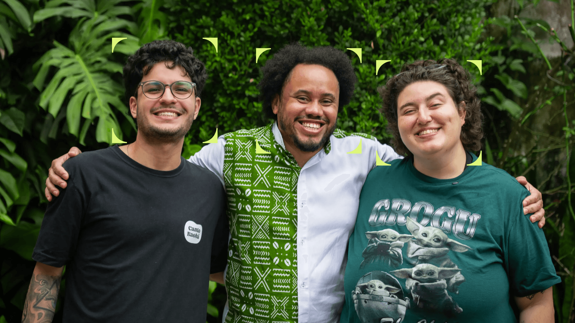 Três fundadores do Canto Baobá, clínica de psicologia parceira da Tivita, sorrindo abraçados em frente a um jardim. Um veste camiseta preta com o logo da clínica, outro usa camisa com estampa africana em verde e branco, e a terceira veste camiseta verde.