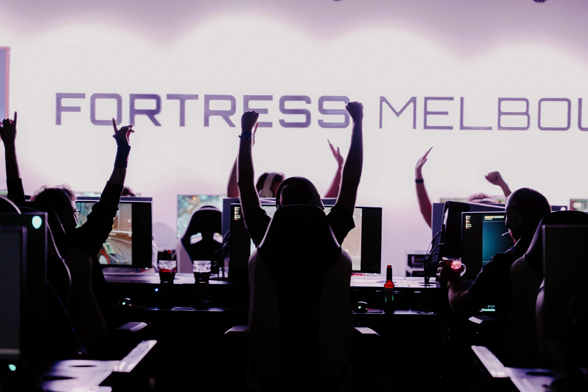 A group of people playing on the computer with their arms in the air in celebration