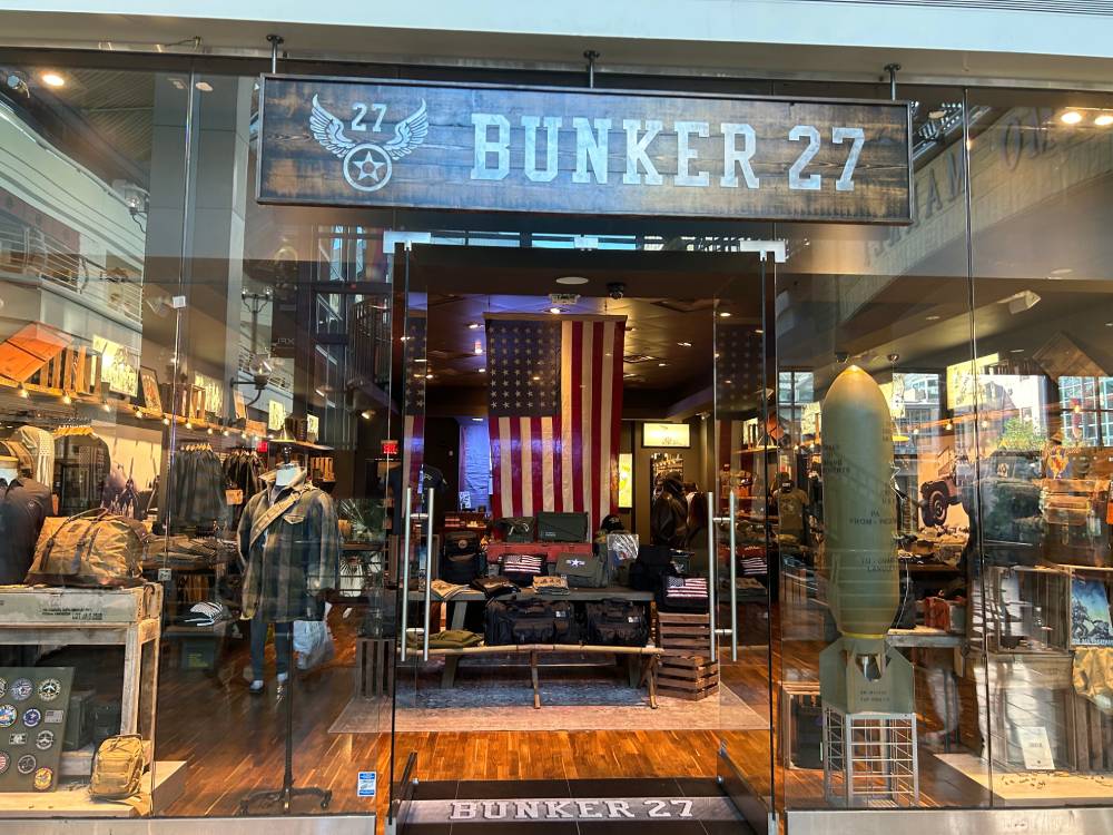 Bunker 27 storefront with a wood-plank sign, military surplus gear displays, and a large American flag inside
