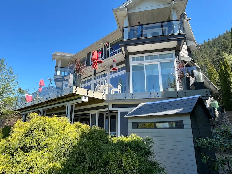 Three-storey hillside home featuring frameless glass railings on multiple balconies and decks, offering modern design and open outdoor views in Vancouver, BC.
