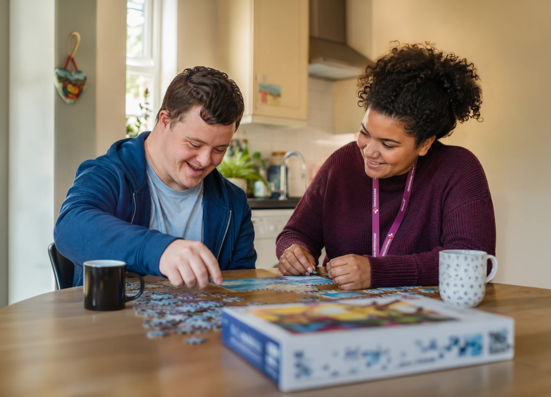 Newcross care professional supporting a young man with a learning disability to complete a jigsaw puzzle together at his kitchen table.
