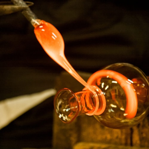 玻璃吹制过程特写：熔炉中炽热的橙色熔融玻璃被拉出并塑形。