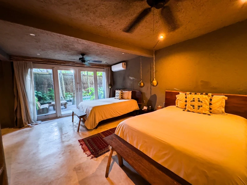 Two Bedroom Villa with Pool at Nômade Tulum highlighting large bed with pillows, ceiling fan, chair, and decorative furniture.