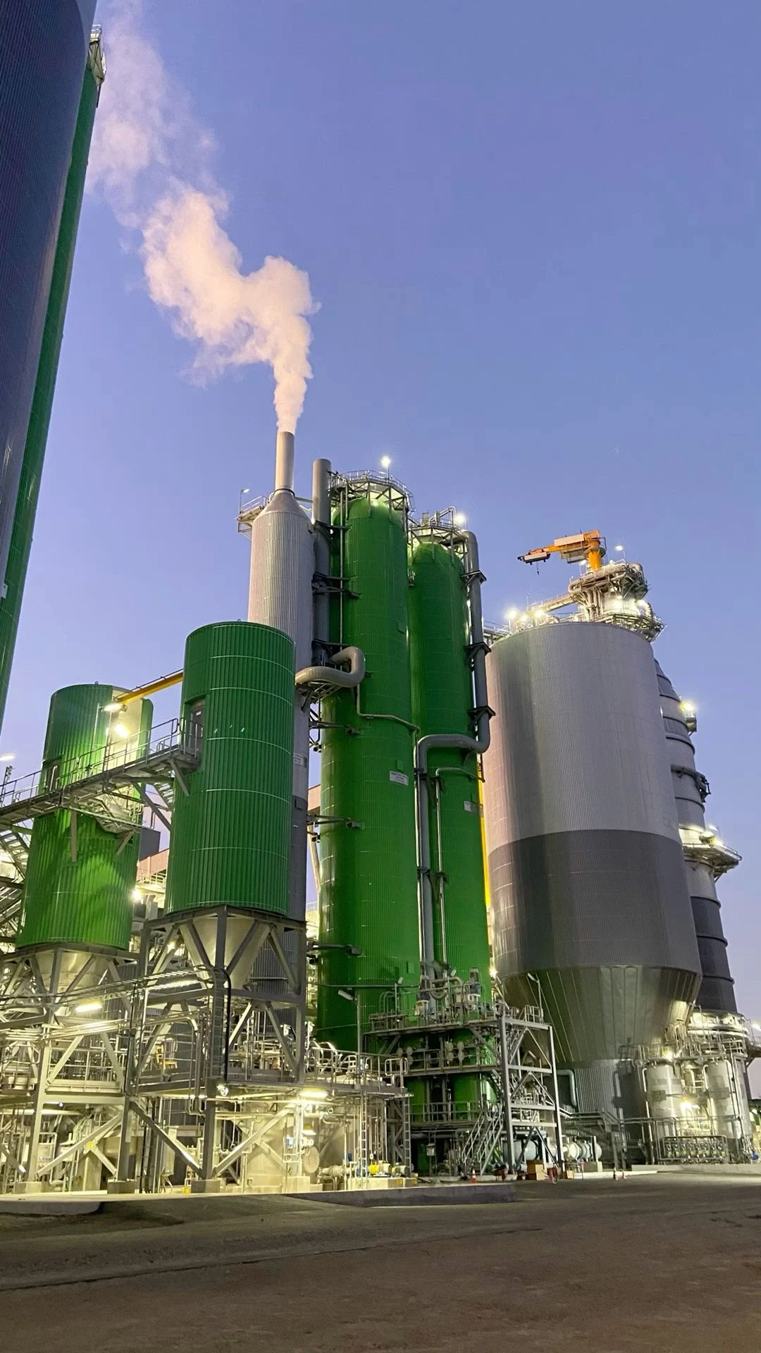 Industrial plant with green silos at dusk