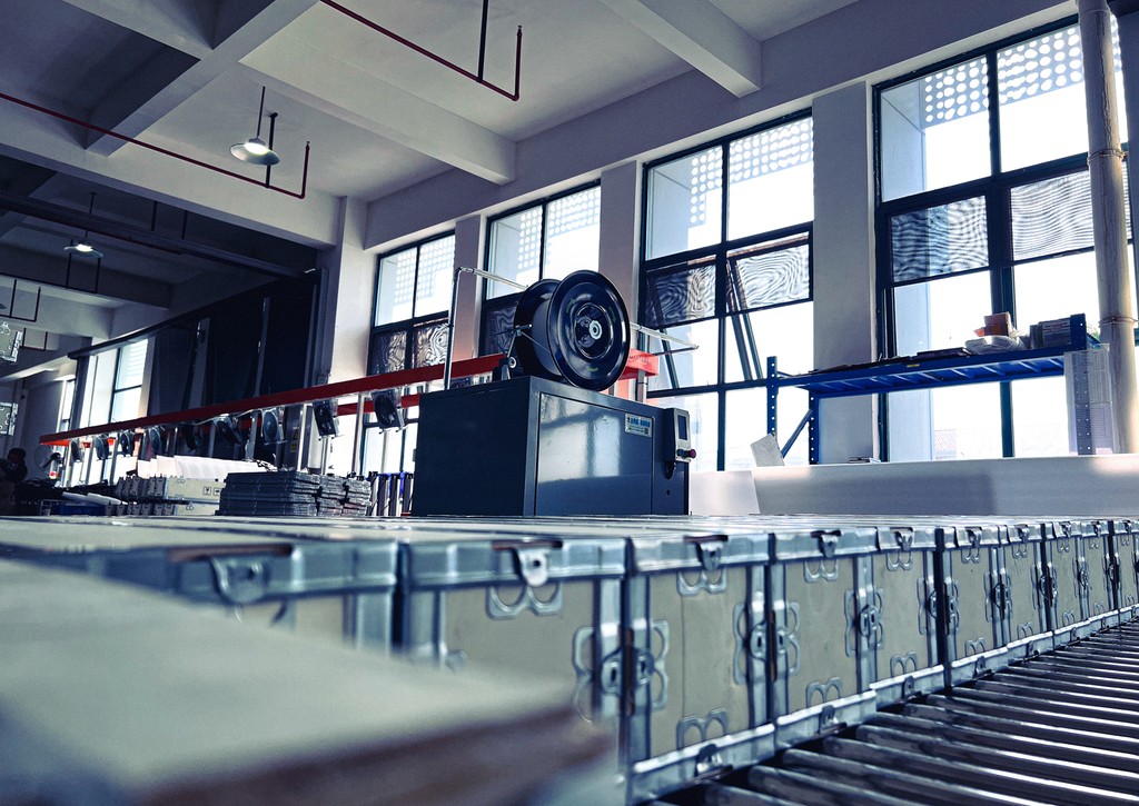 A row of metal boxes moves along a roller conveyor belt in solar water pump factory