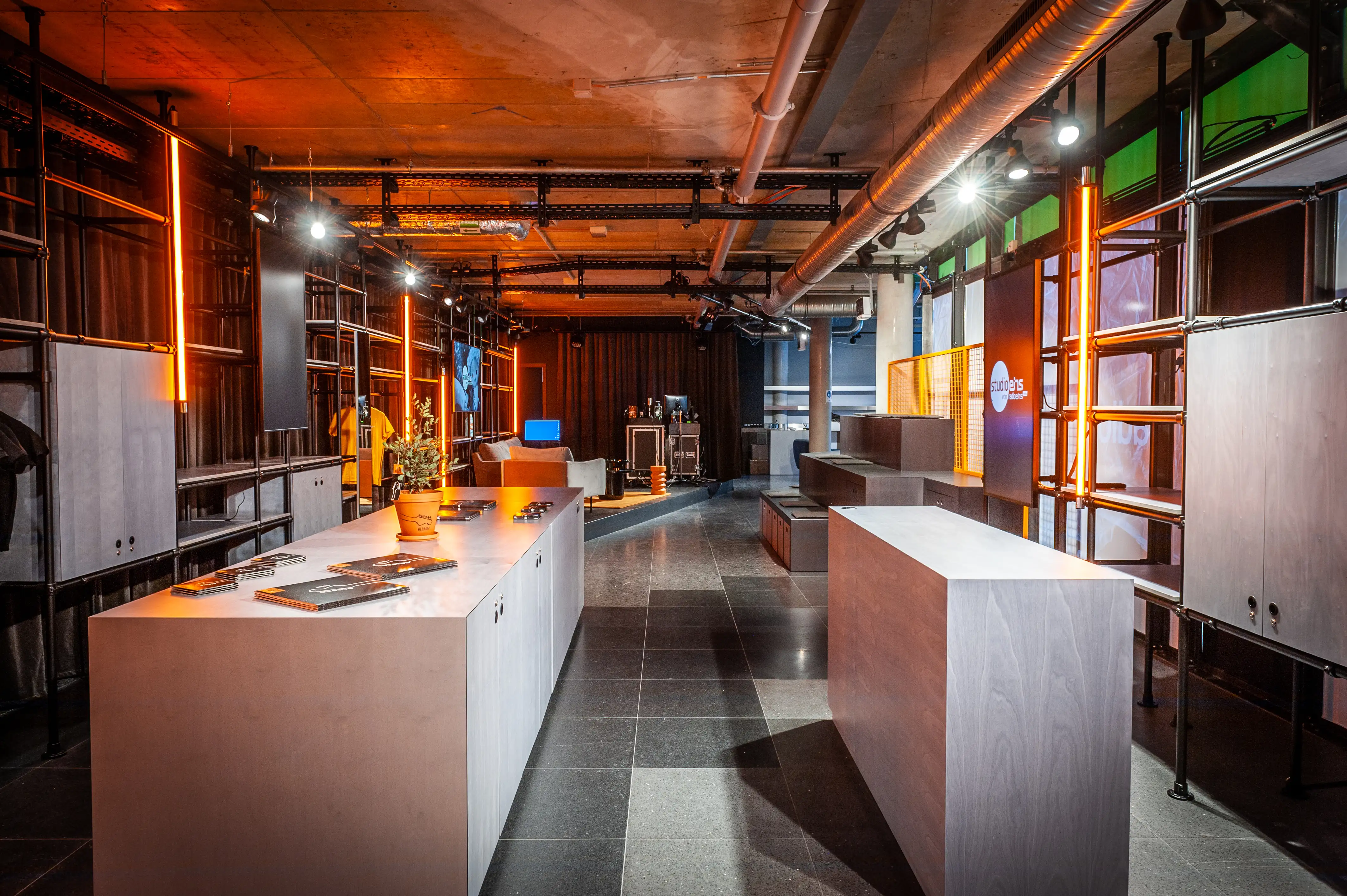 Studio interior with light wood counters, dark stone floor and orange-lit scaffold shelving at Radio Eins.