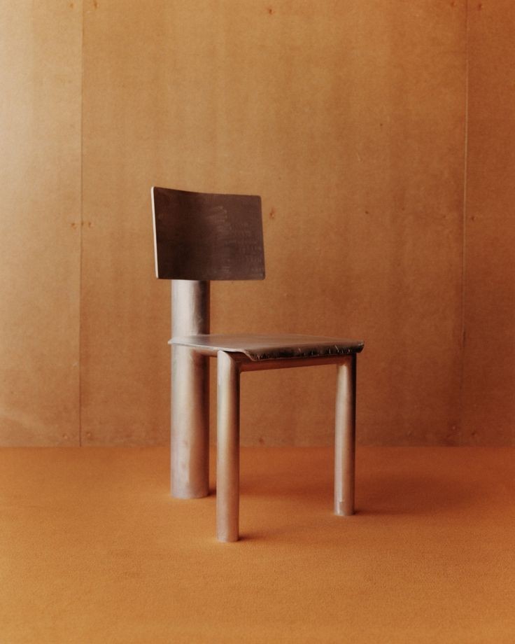 a photo showing a three-legged chair against a wall in the color of natural wood, the floor in the same shade