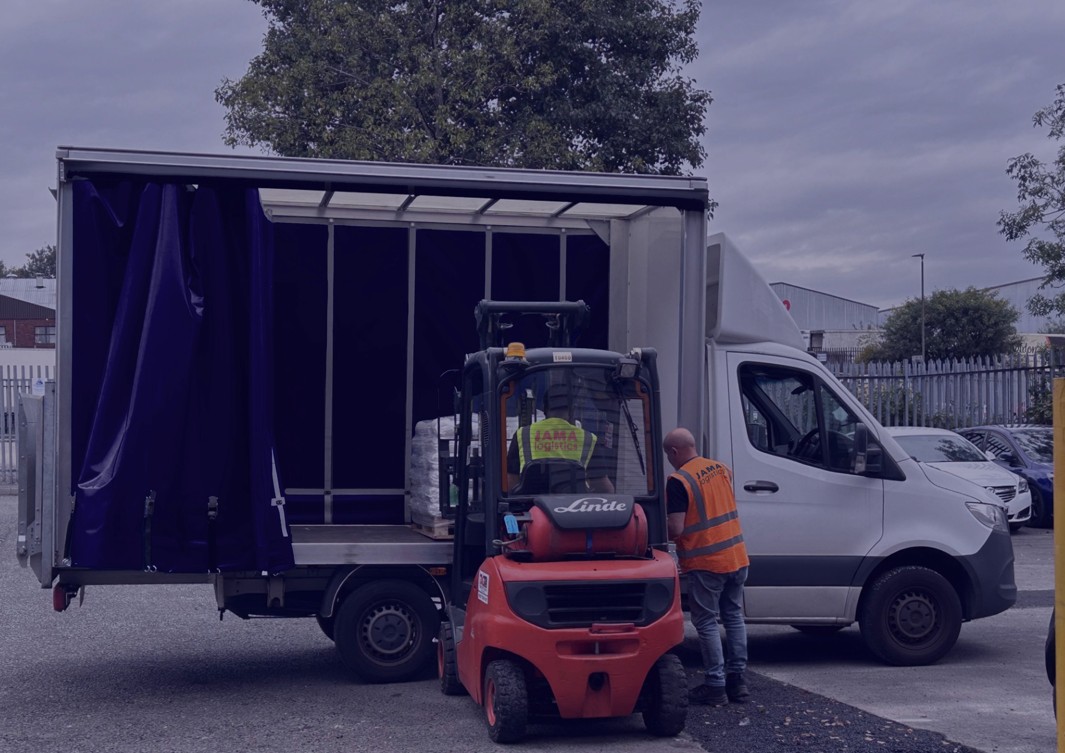 Image of a forklift laoding a Luton Van with a pallet and two men wearing high vis in the middle of a loading bay