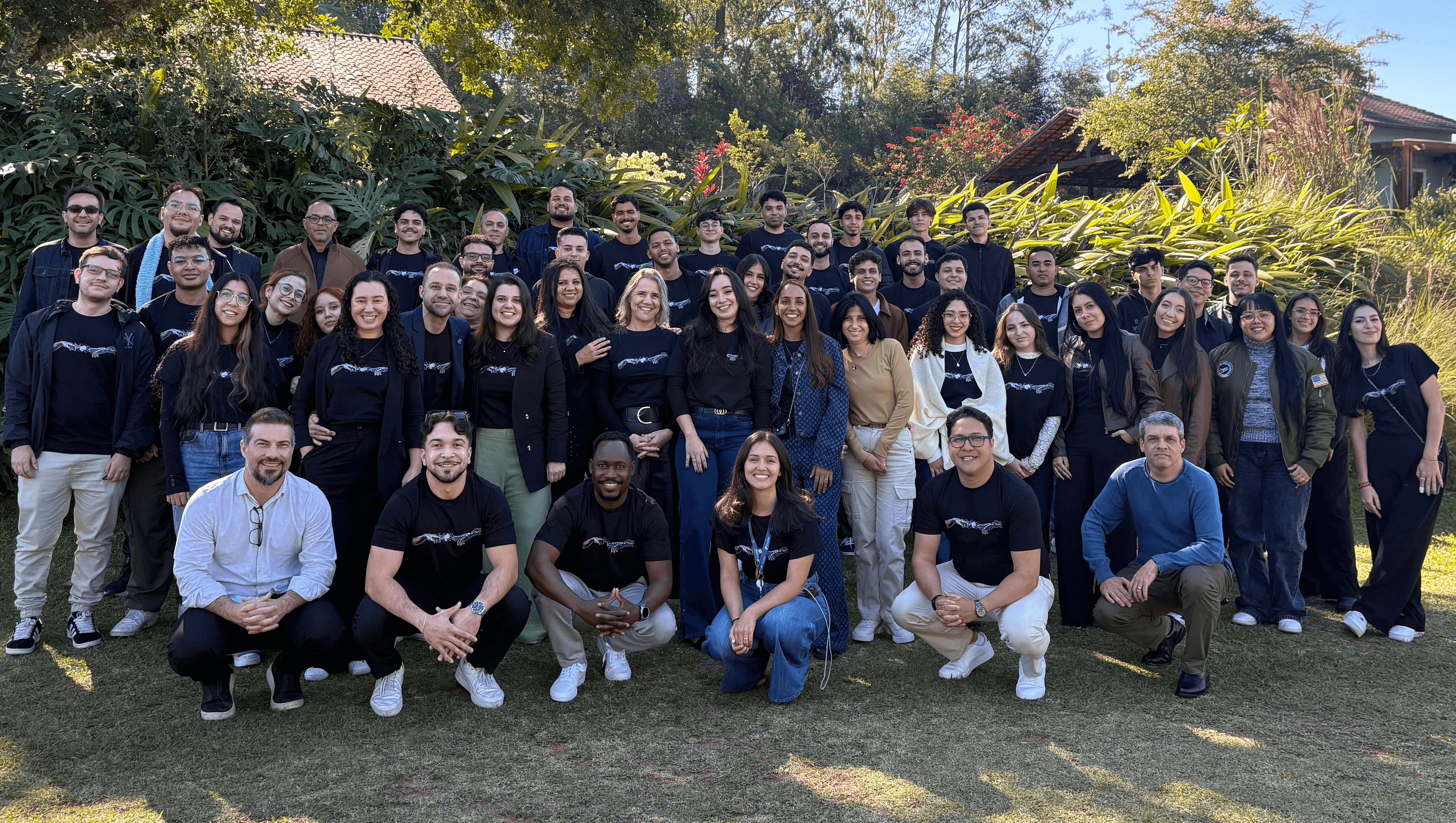 Grupo grande de pessoas sorrindo ao ar livre em frente a plantas.