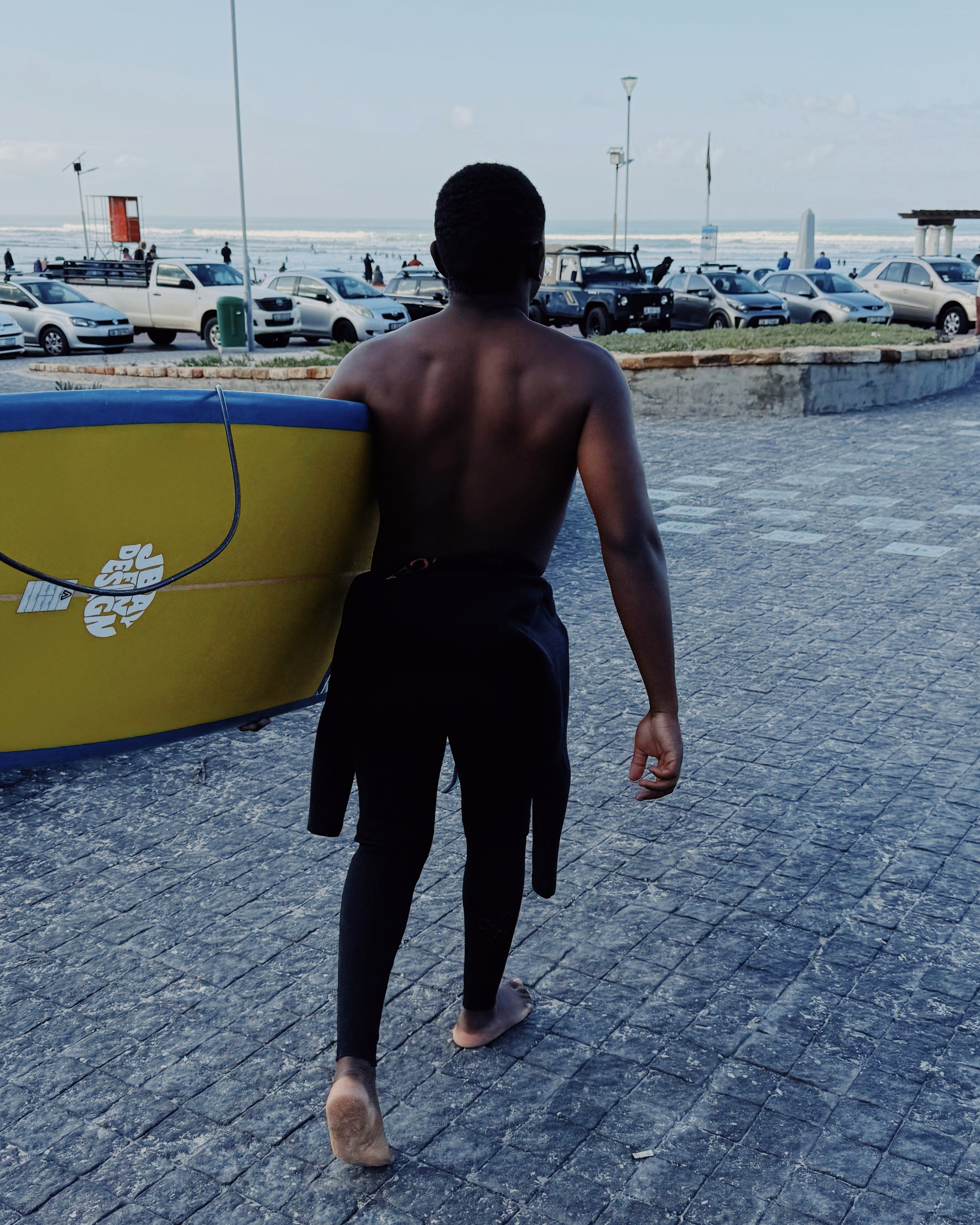 A male surfer carrying his longboard to head to the beach for a surf session in Muizenberg, Cape Town