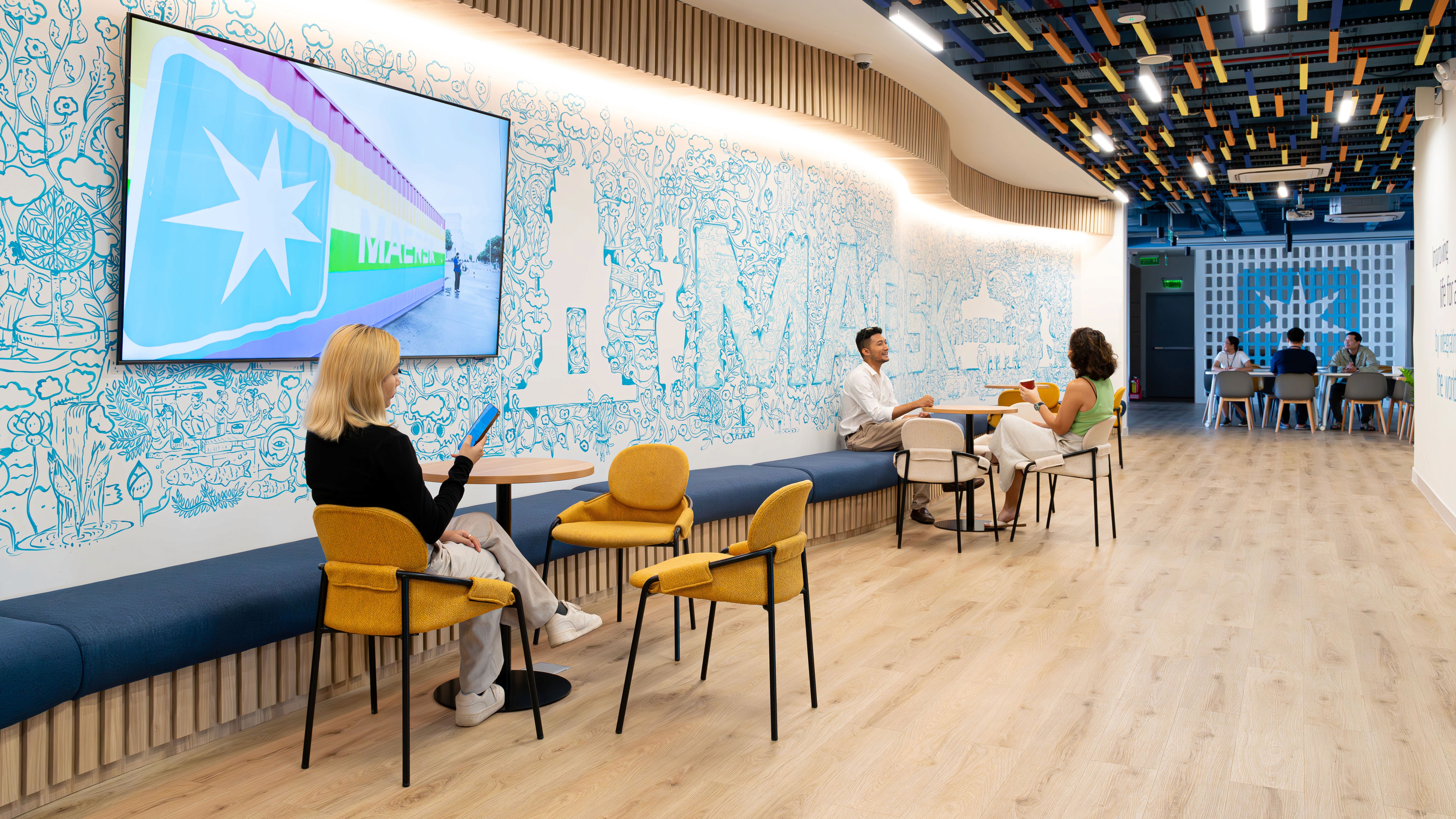 Circulation corridor with large-scale Maersk container graphic wall, integrated seating, and informal meeting points enhancing brand storytelling