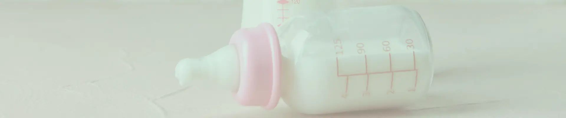 Two baby feeding bottles filled with milk, lying on a white surface, each with a soft pink screw-on cap.