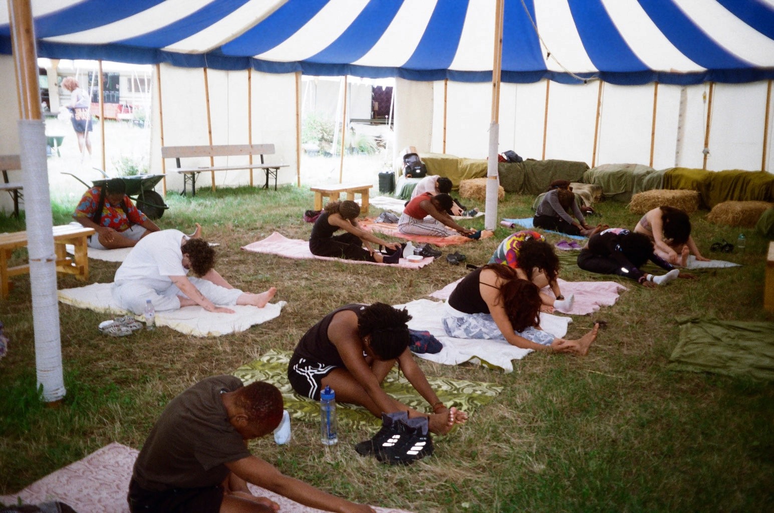 A group of people stretch in yoga positions under a canopy tent