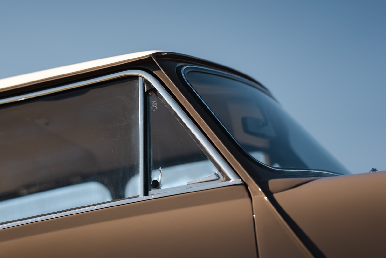 Close-up of a vintage car's roof and side window against a clear blue sky.