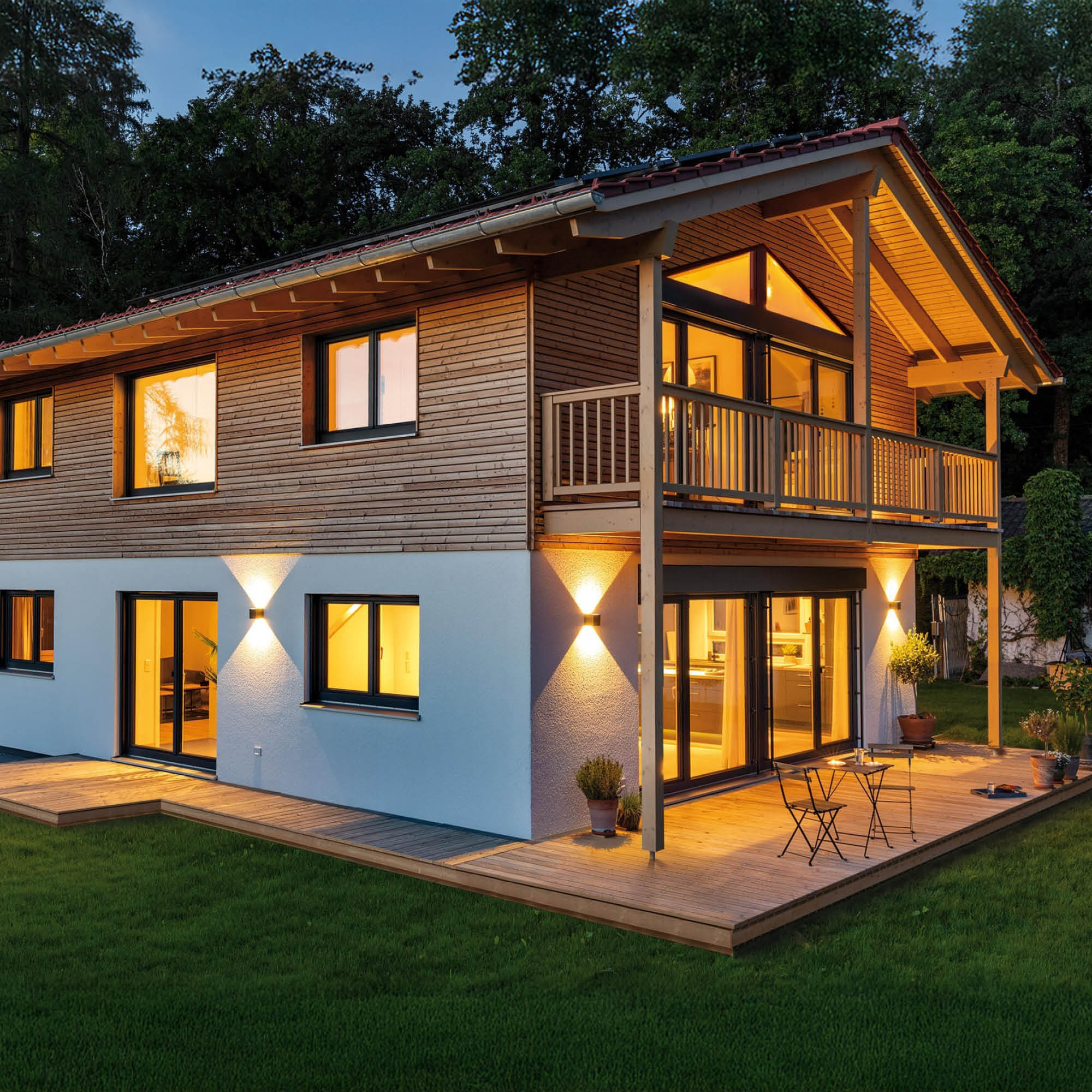 Modernes Holzhaus mit großer Terrasse und Garten bei Dämmerung beleuchtet.