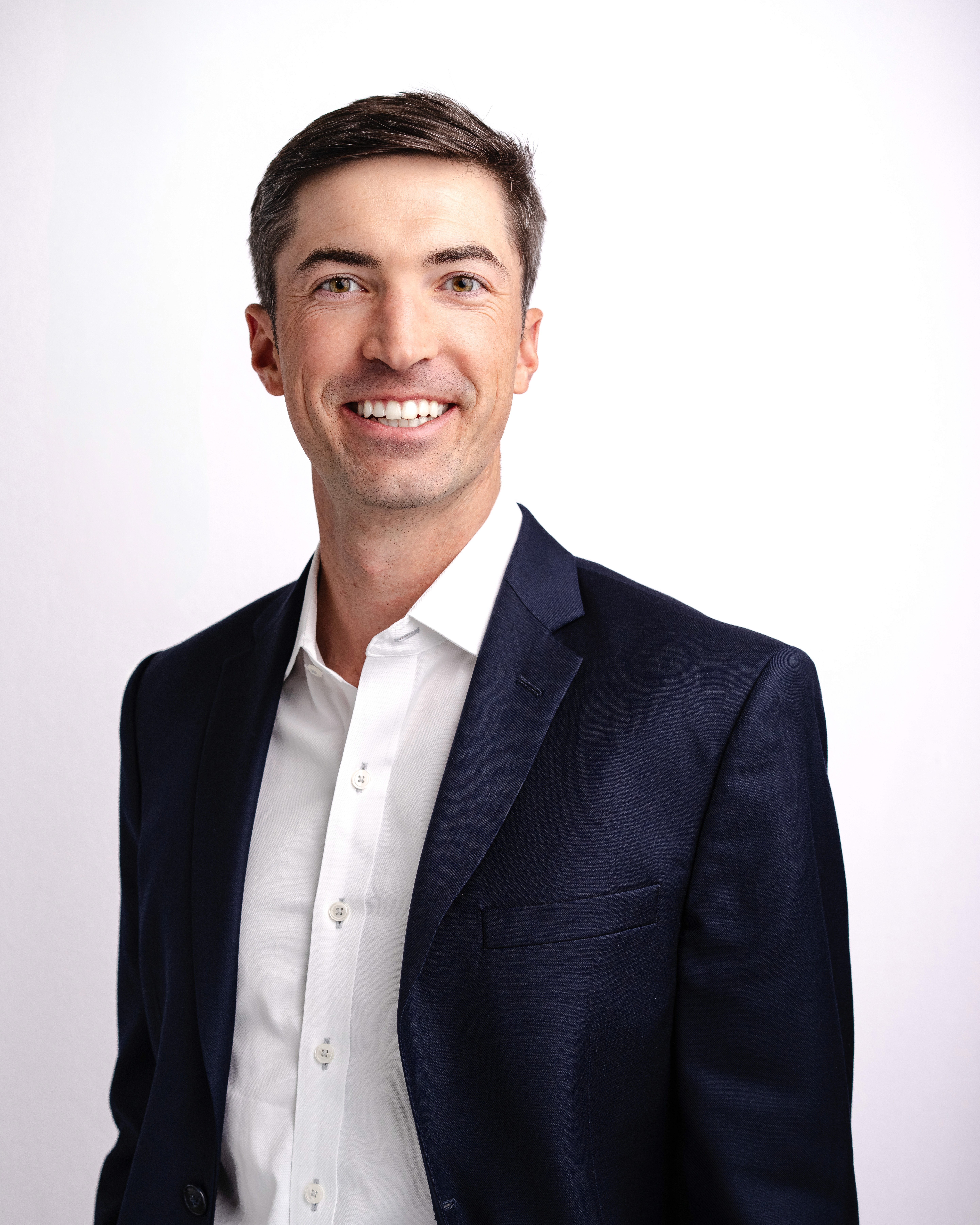 Professional headshot of Levi Pettit, CFA, founder of Dornick Wealth Management, wearing a navy suit and white shirt, smiling in front of a white background