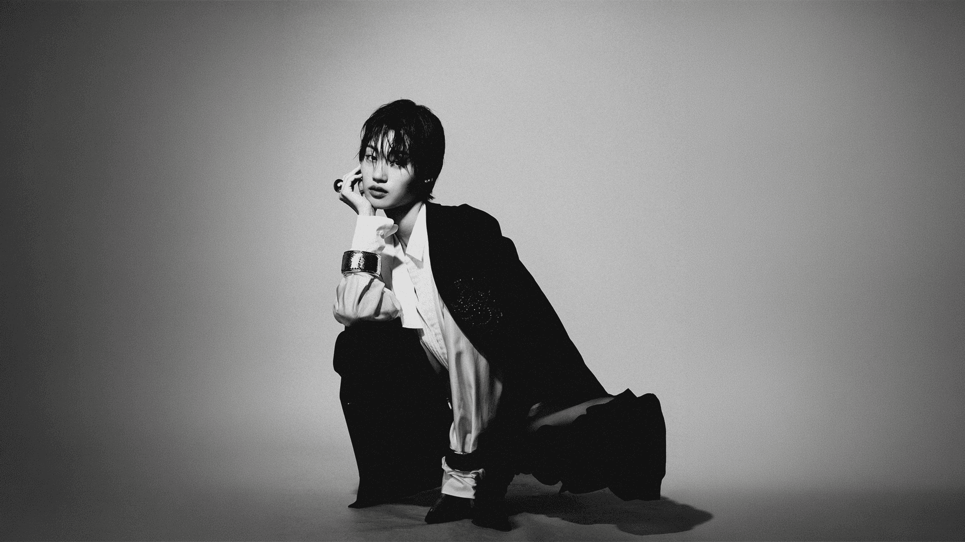 Full-body black and white editorial shot of Jihoon crouching and looking at the camera