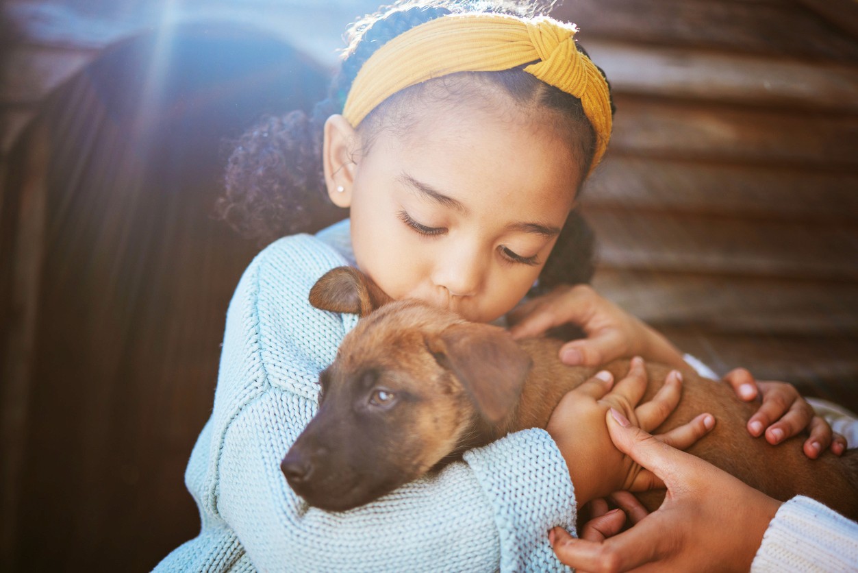 little girl holding and kissing puppy