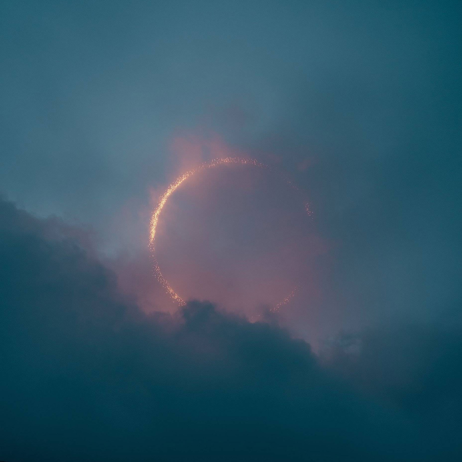 Fiery ring, possibly a solar eclipse, surrounded by dark clouds.