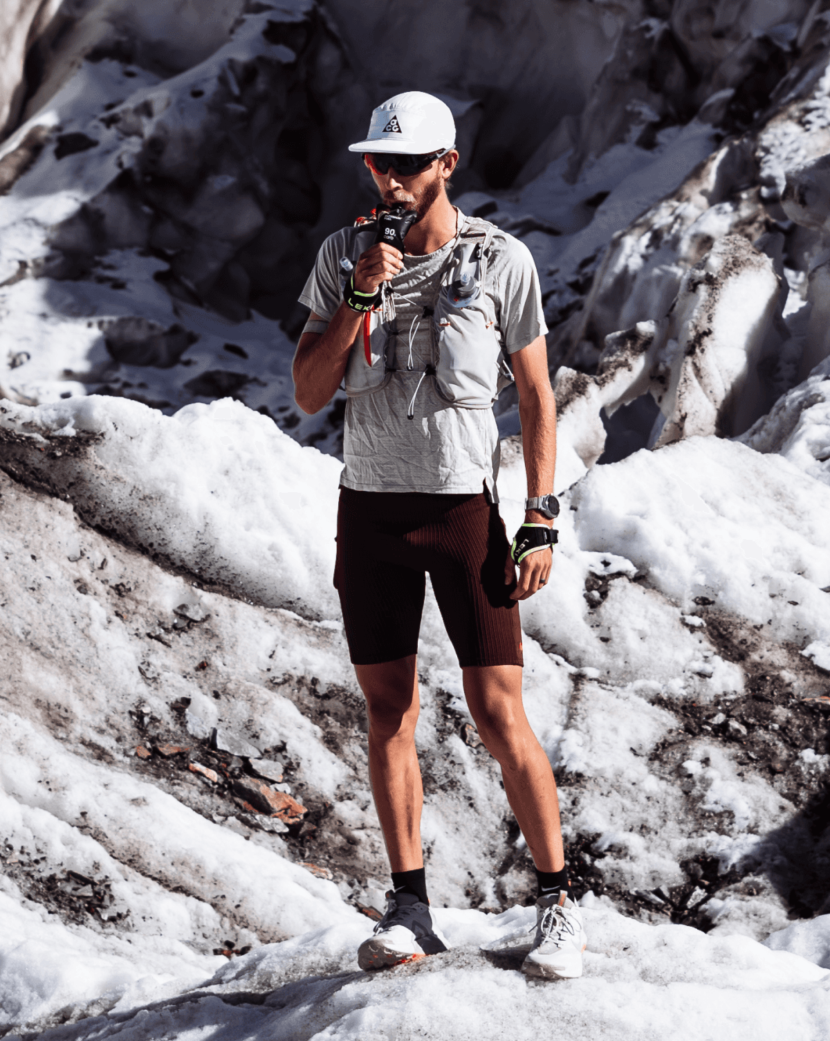 Caleb drinking from a bottle while standing on a snowy mountain trail.