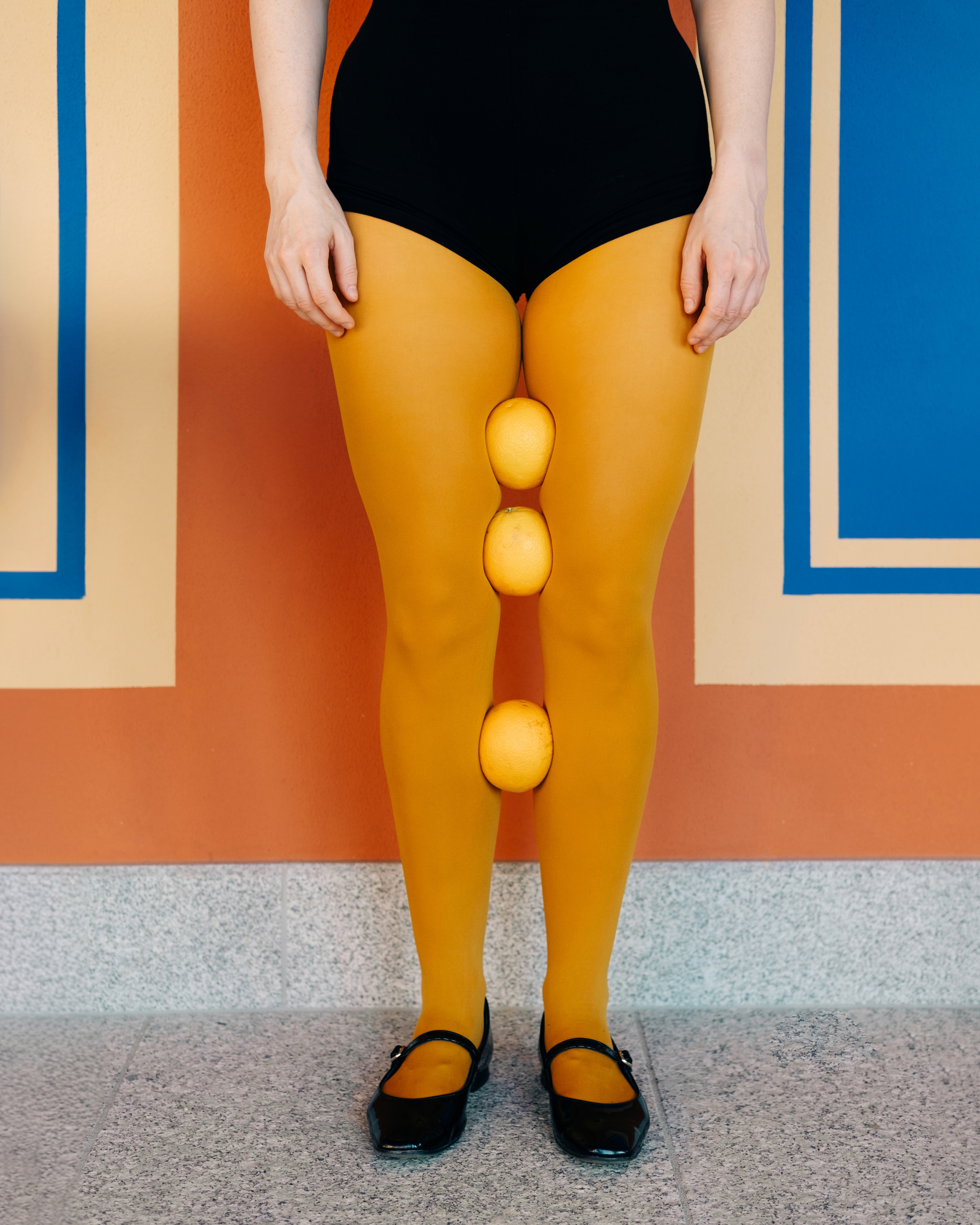 Gosia – Bitter Sweet – playful conceptual shot with citrus fruits balanced between mustard tights