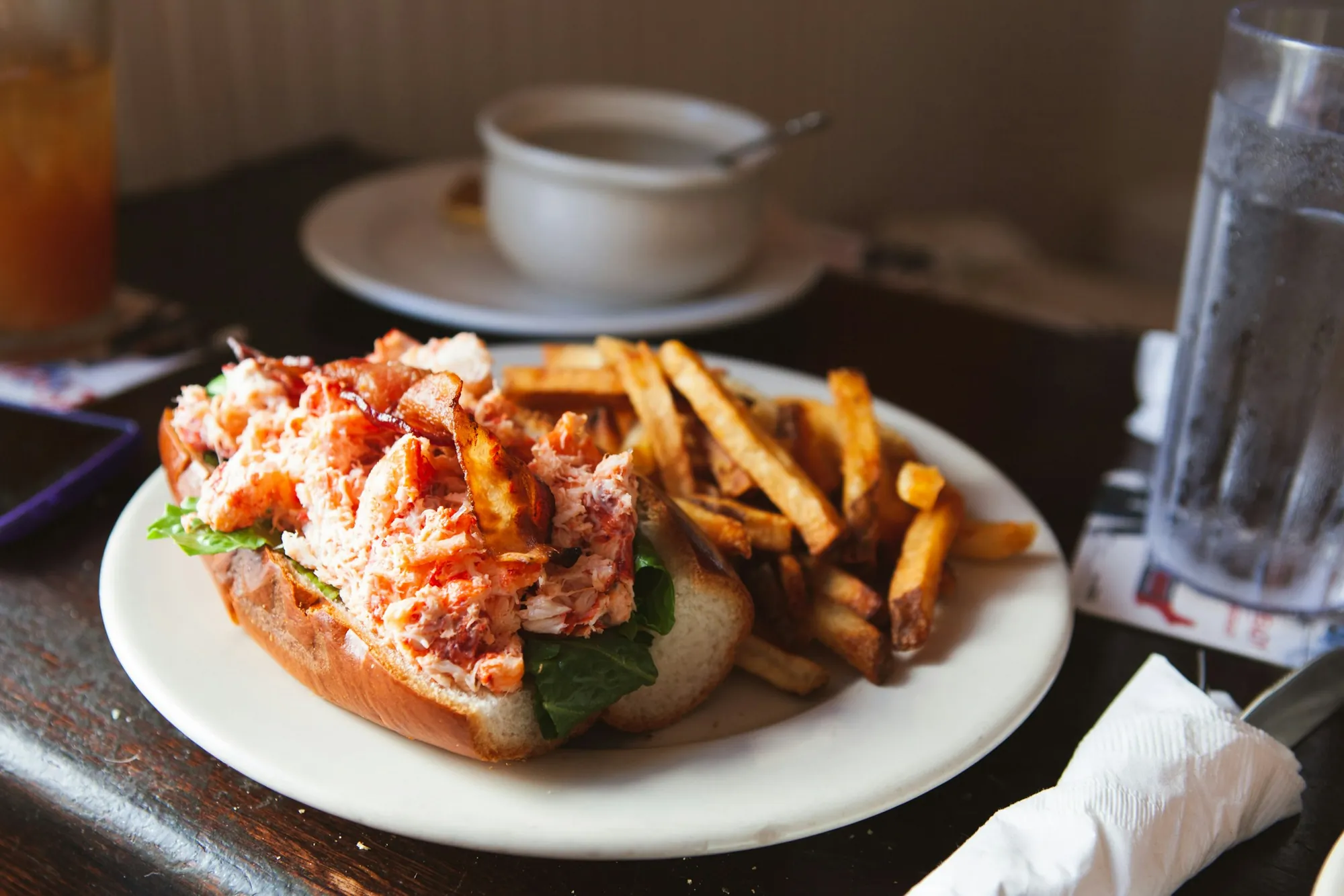 A loaded lobster roll on a plate with a side of fries
