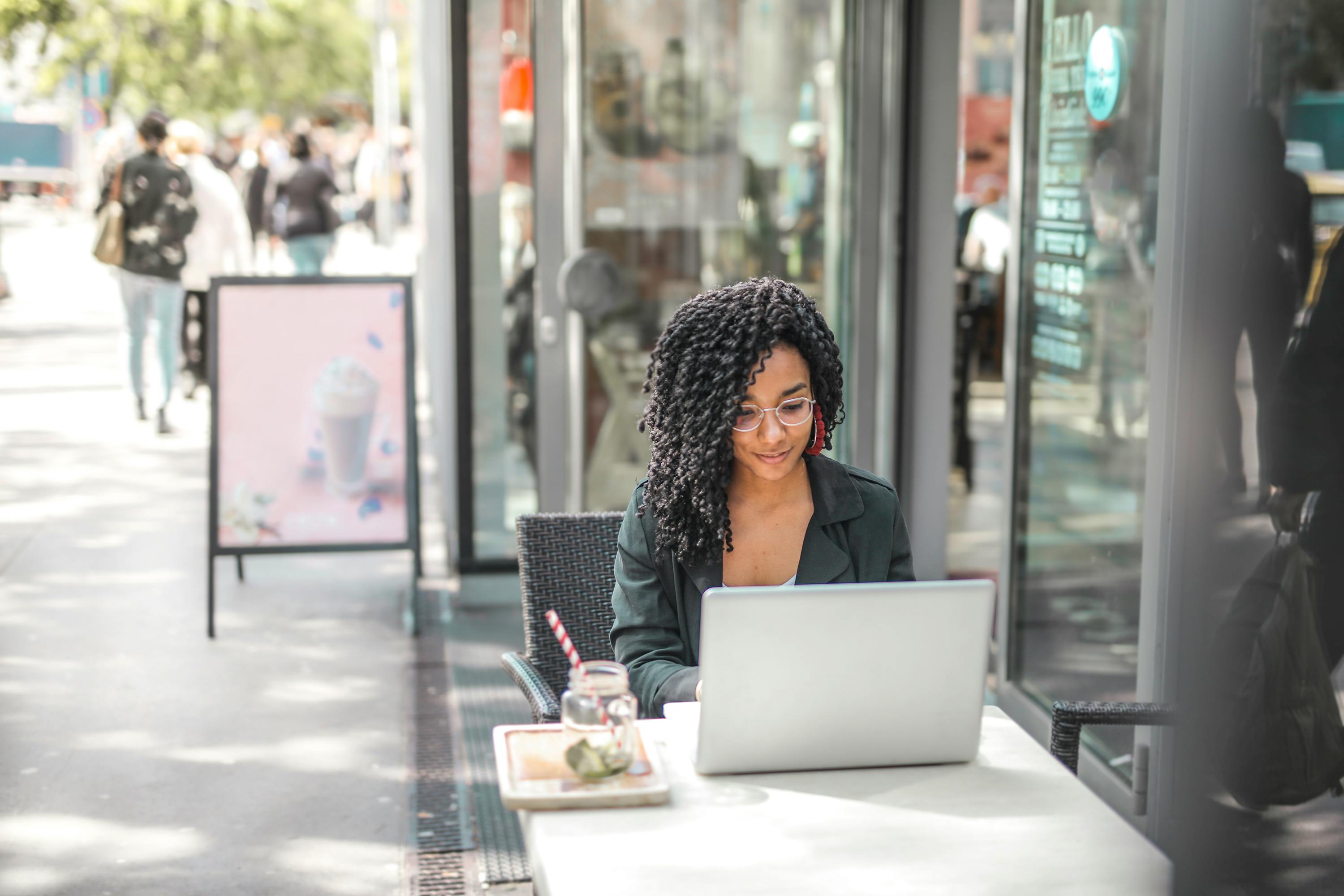 Young woman using laptop while having tasty beverage in modern street cafe