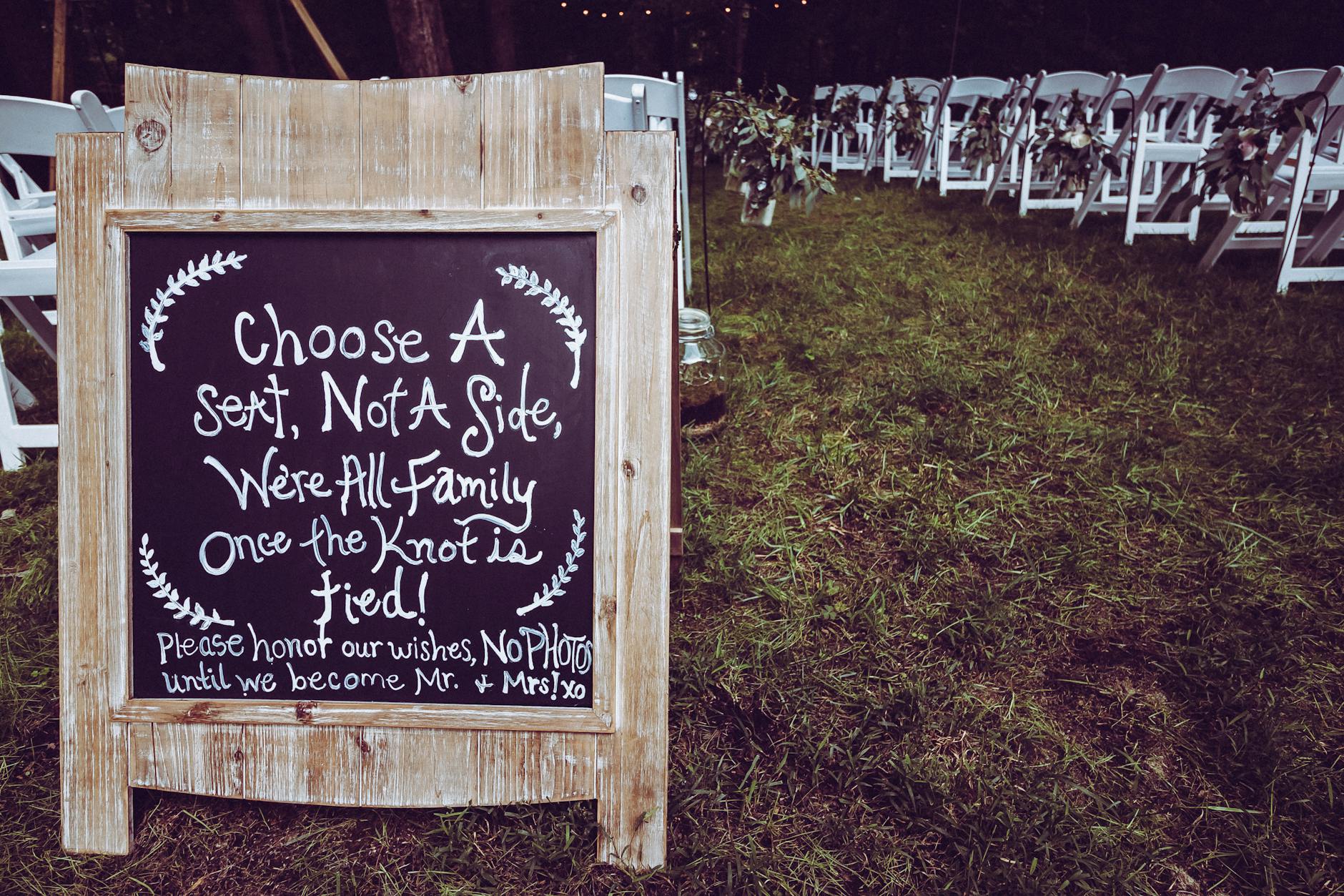 Charming outdoor wedding ceremony with sign and chairs under a canopy.