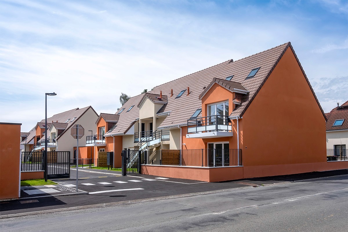 Maisons en rangées avec des façades orange, balcons et toits en tuiles, ciel bleu en arrière-plan.