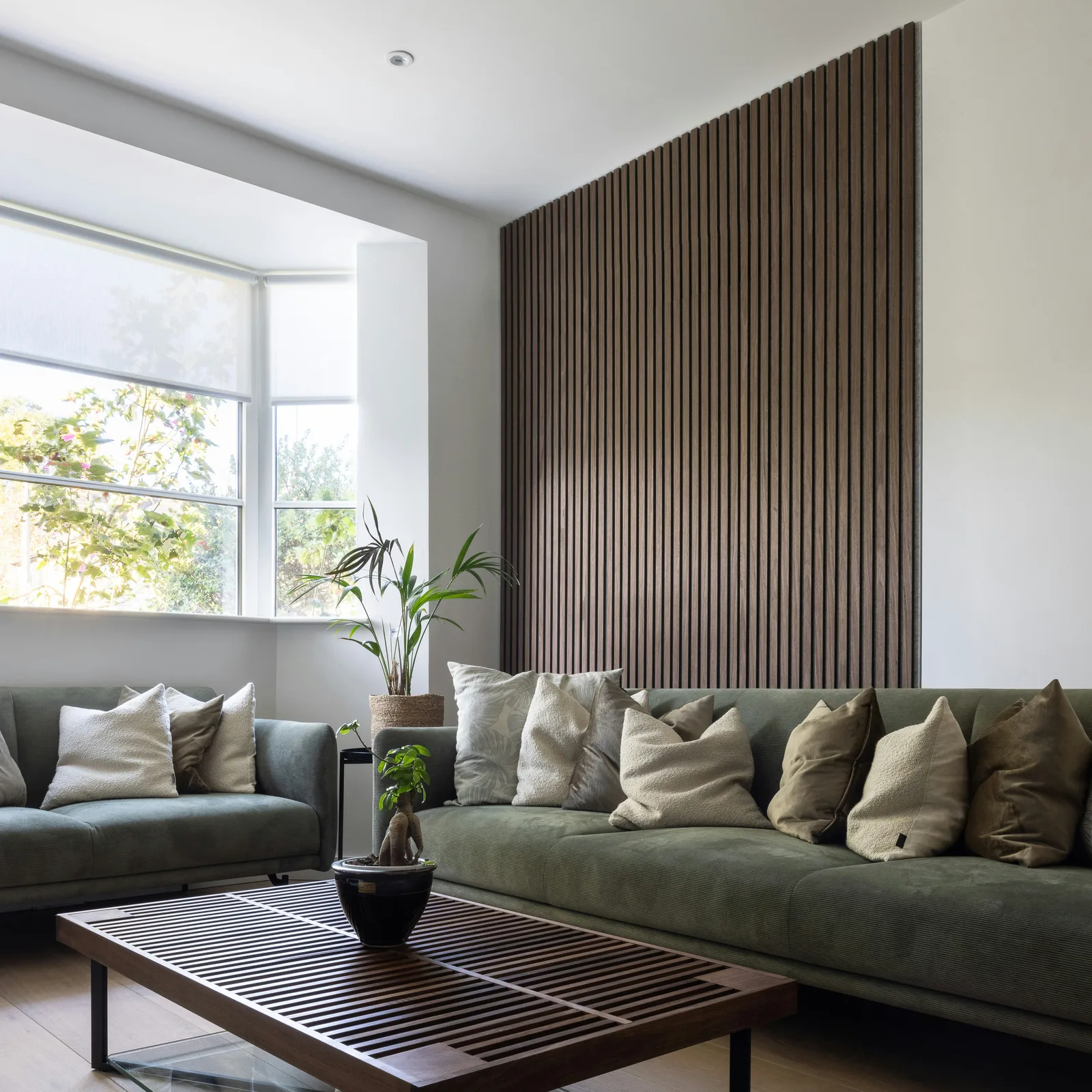 Living room with dark slatted wood accent wall behind green sofas